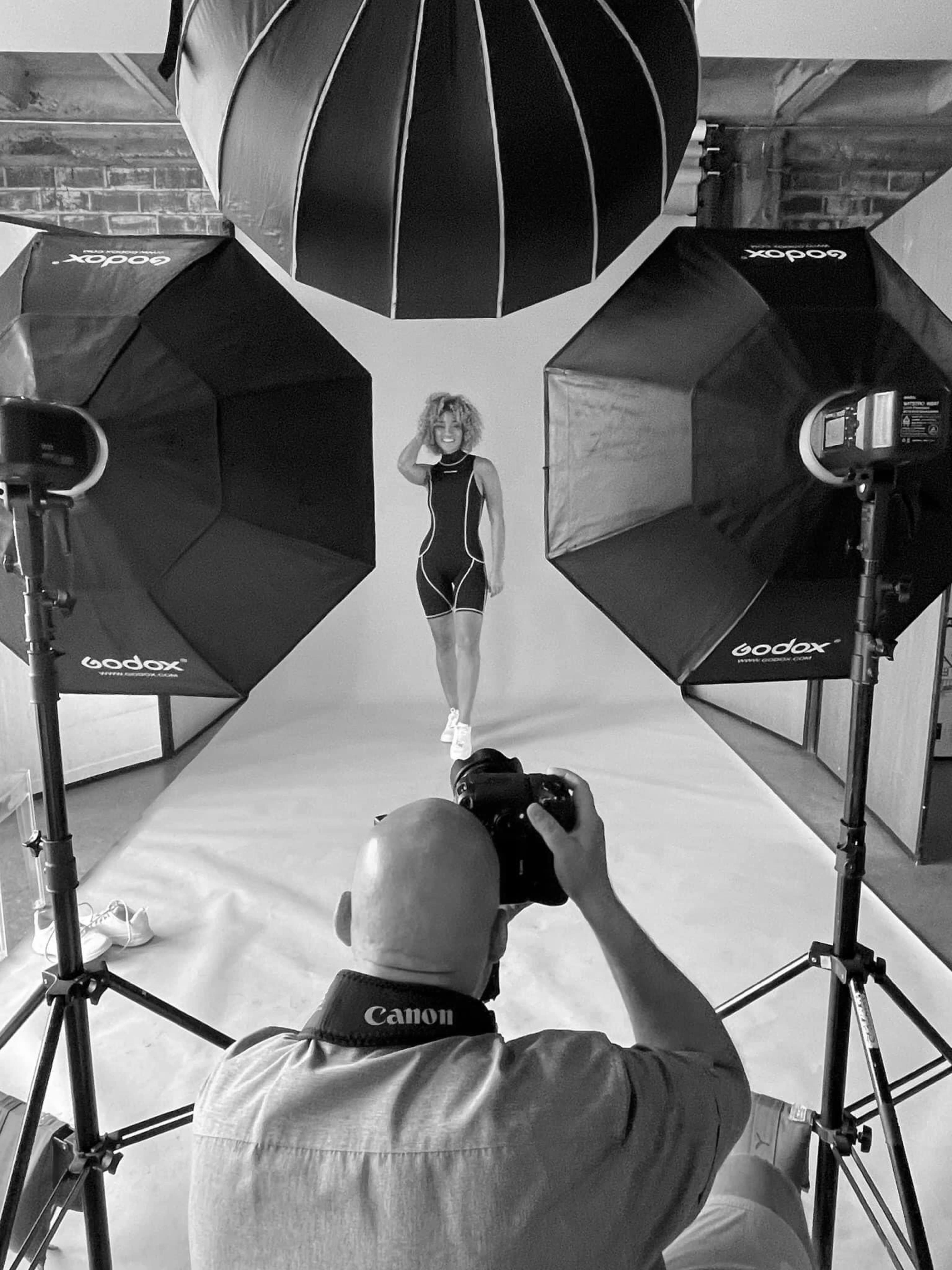 A photographer is taking pictures of a model posed in a studio, surrounded by softbox lighting setups.