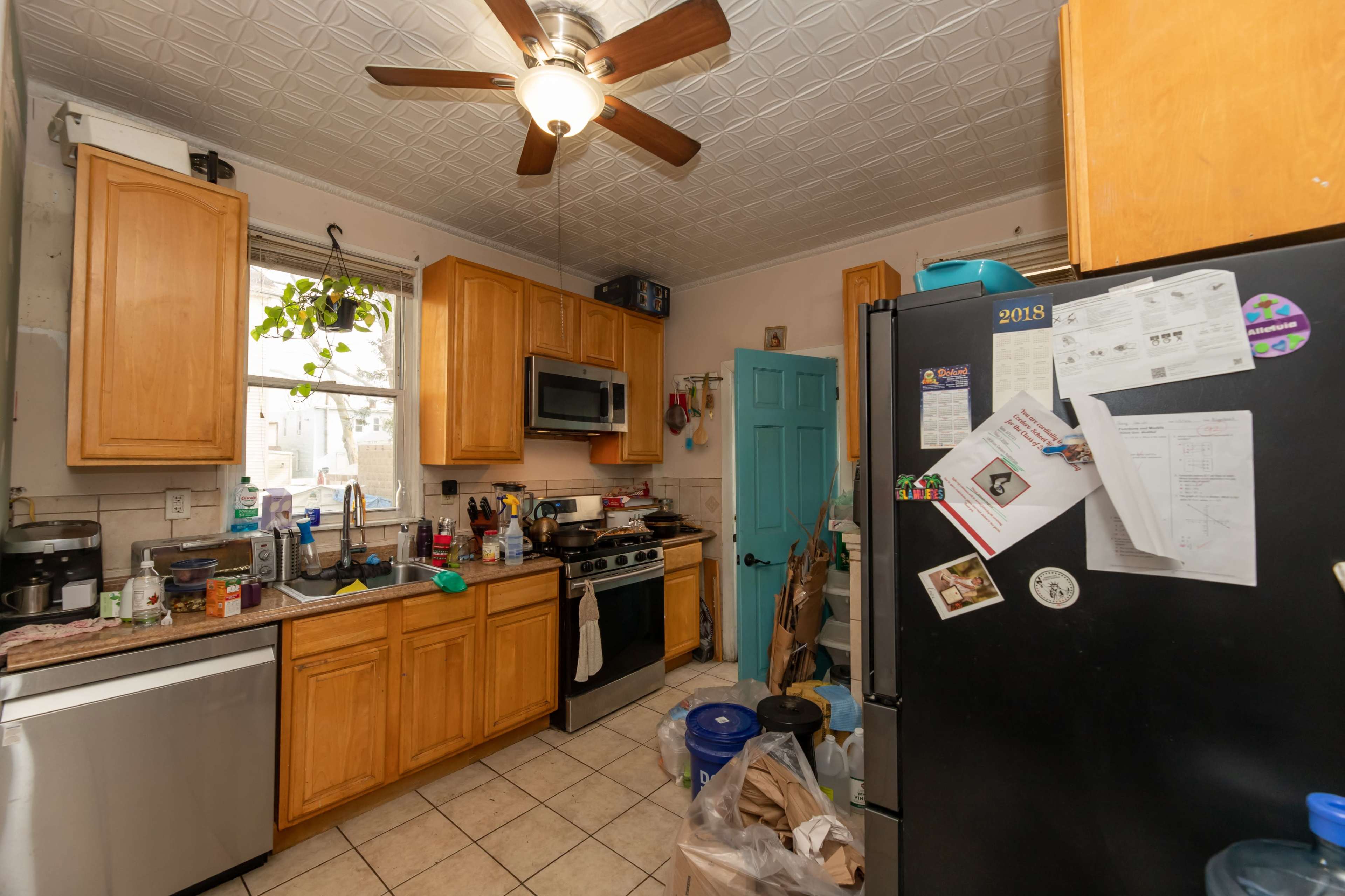 The image shows a kitchen with wooden cabinets, a stainless steel stove, and a cluttered countertop filled with various kitchen items and papers.
