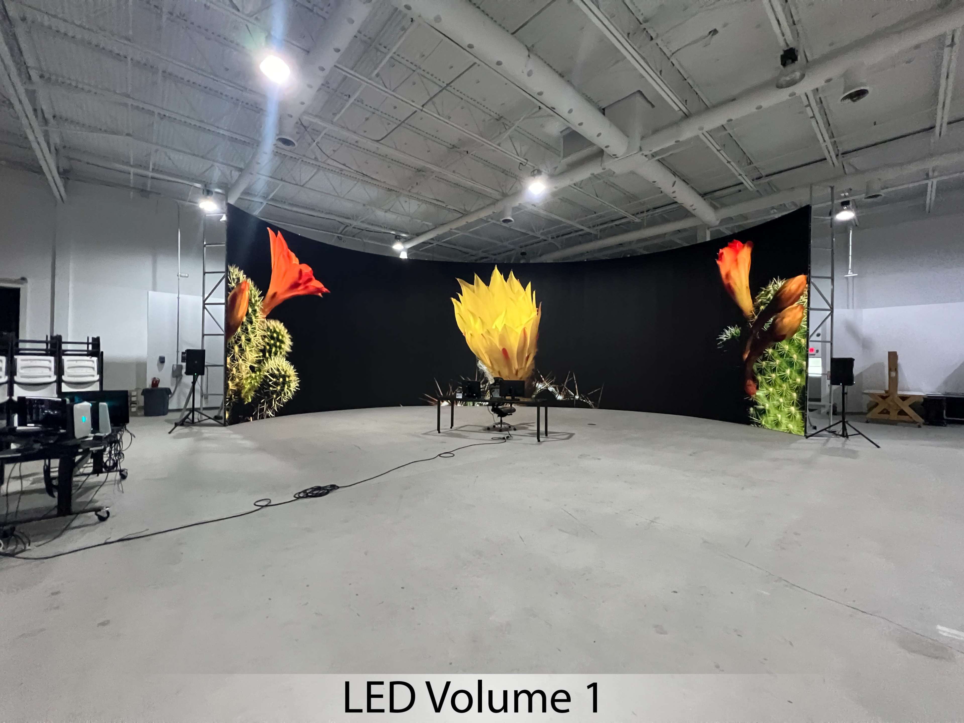 The image shows a spacious studio with a curved LED screen displaying vibrant flower graphics, surrounded by audio equipment and lighting stands.