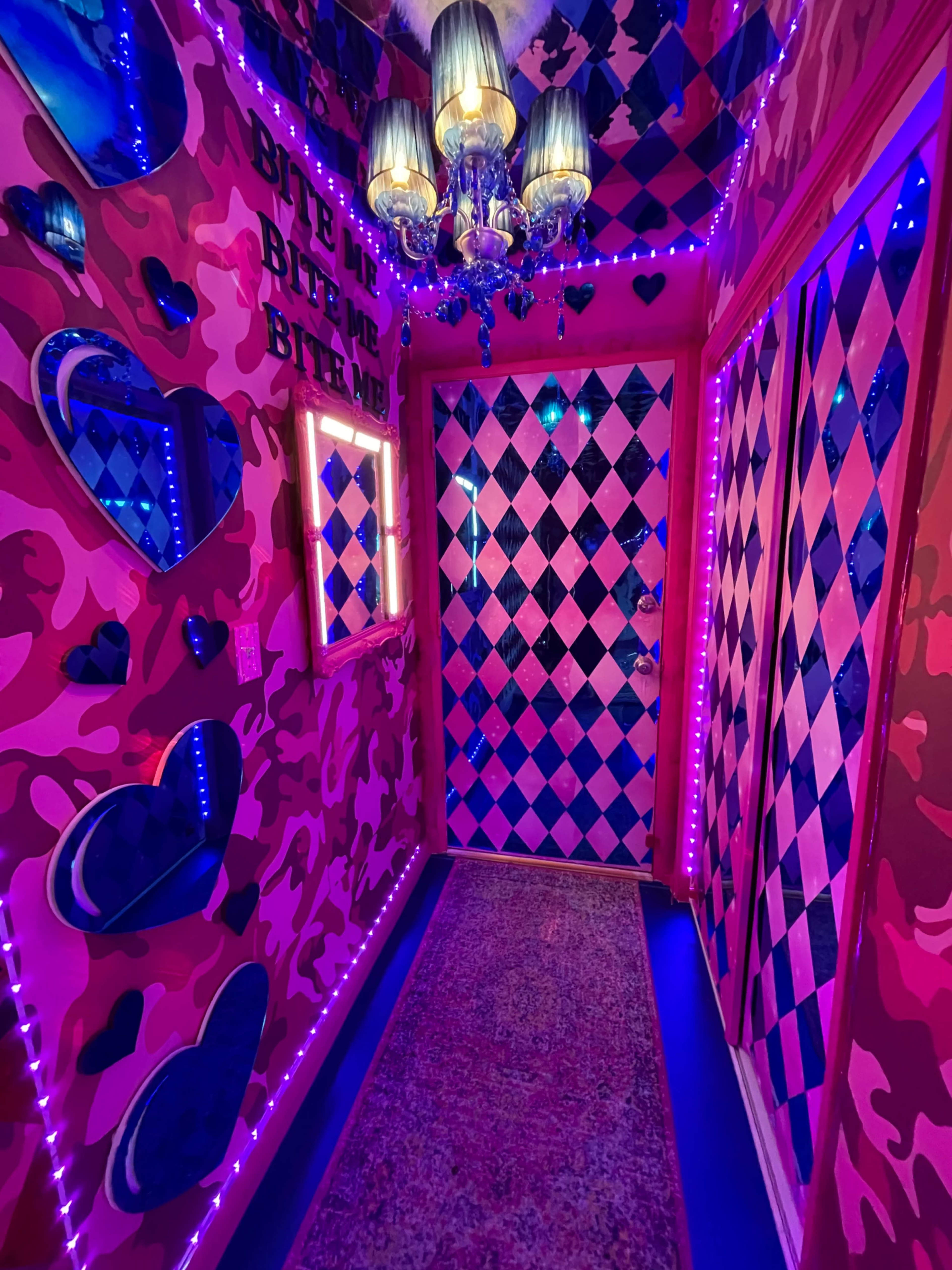 A narrow hallway decorated with pink camo walls, diamond-patterned doors, and illuminated accents.