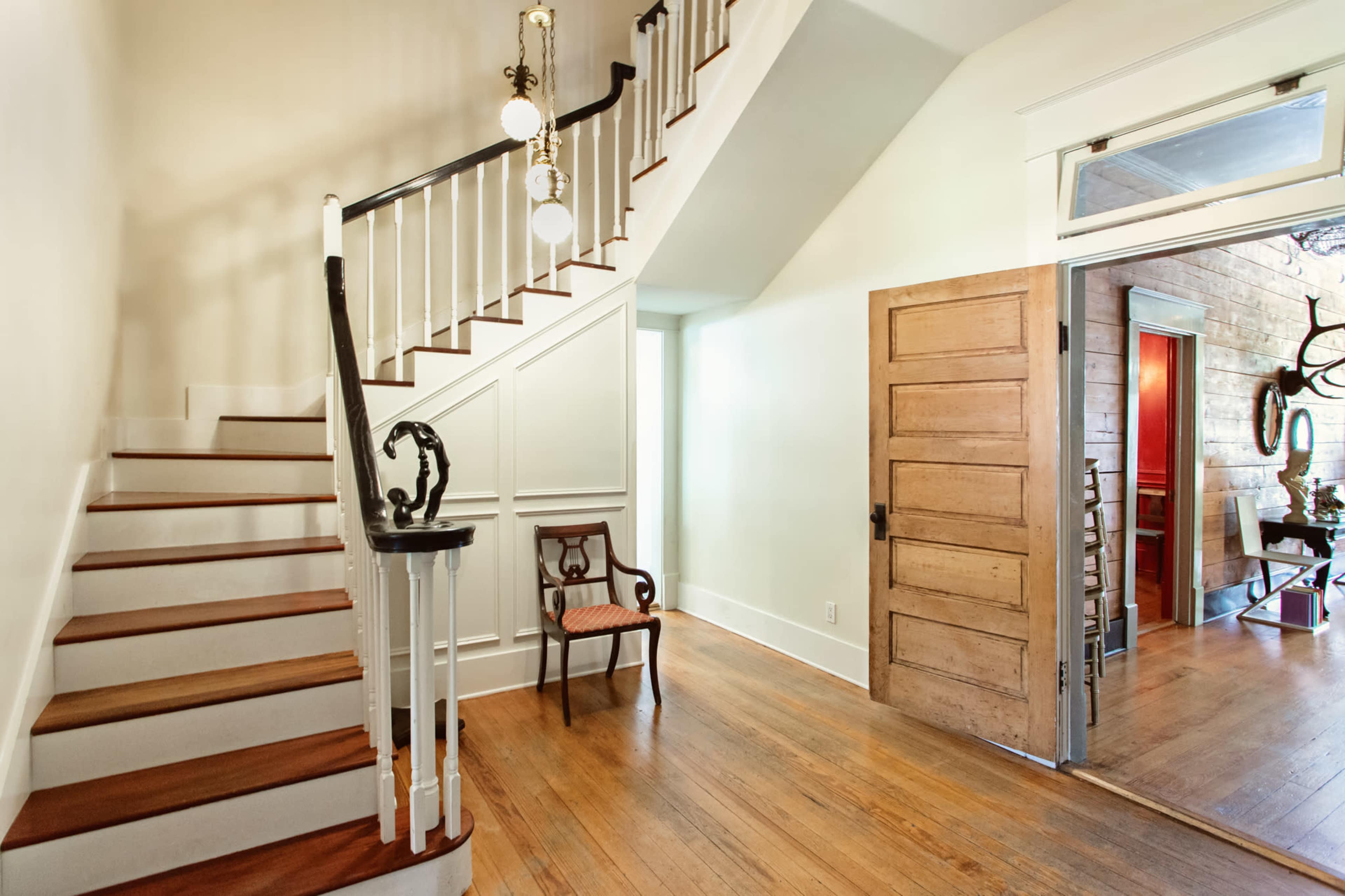 A well-lit entryway with a staircase on the left, a wooden door on the right, and a chair positioned near the entrance.