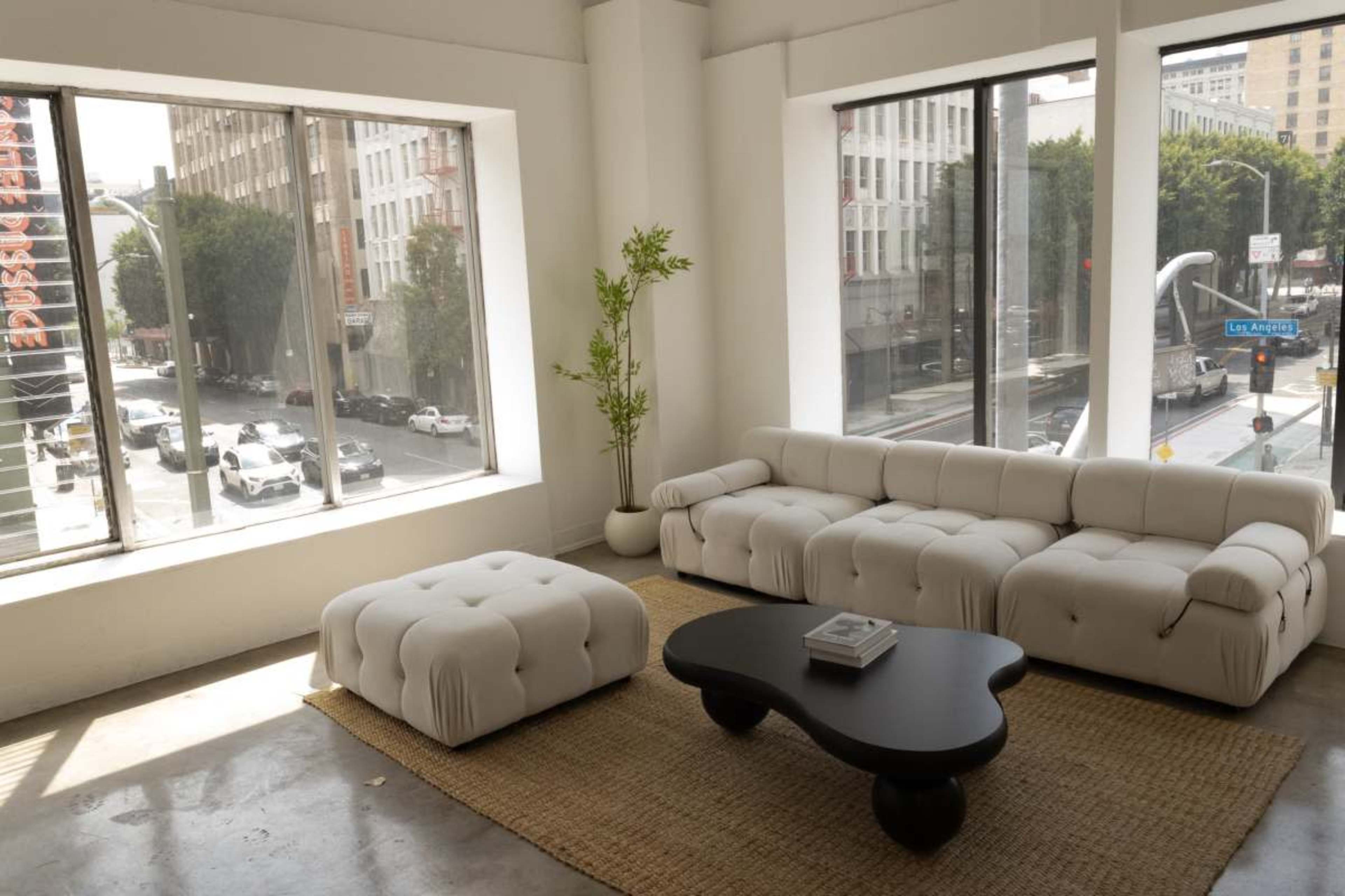A modern living room features a white sectional sofa, a black coffee table, and large windows overlooking a city street.