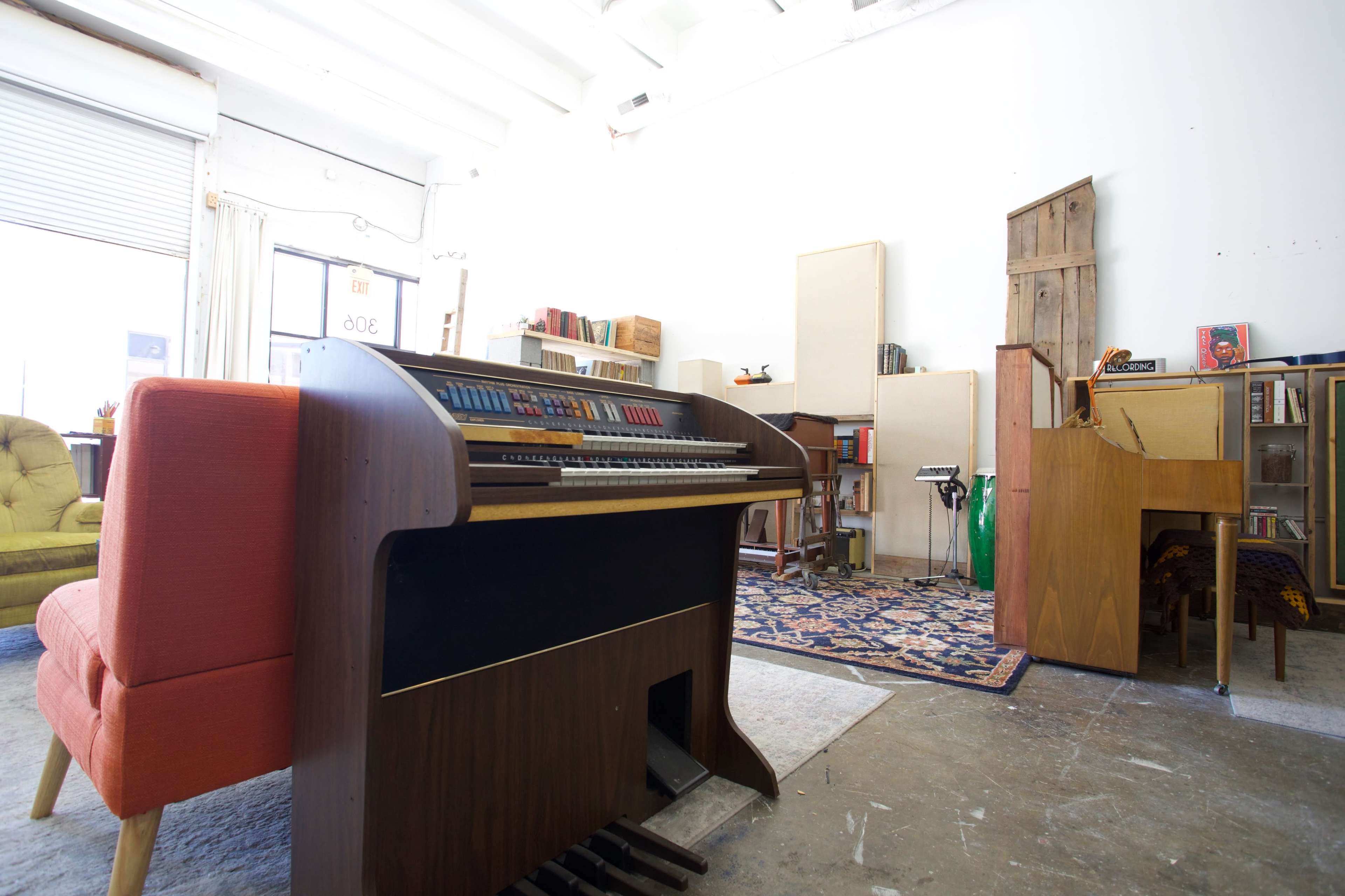 A spacious room with two vintage keyboards, a colorful armchair, and shelves filled with books and decorative items.