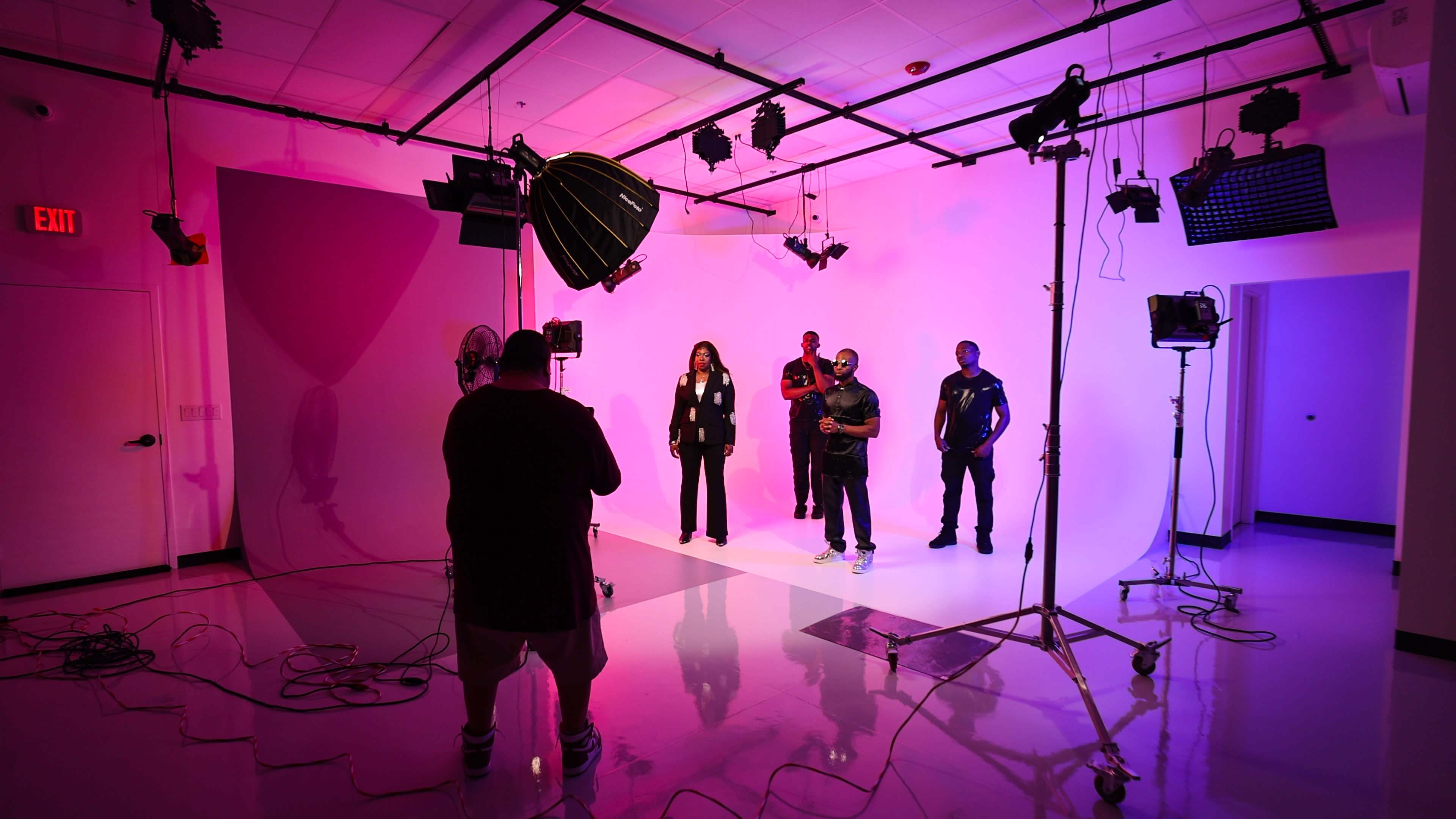 A group of individuals in formal attire poses in a photography studio with multiple lighting setups and a brightly colored backdrop.