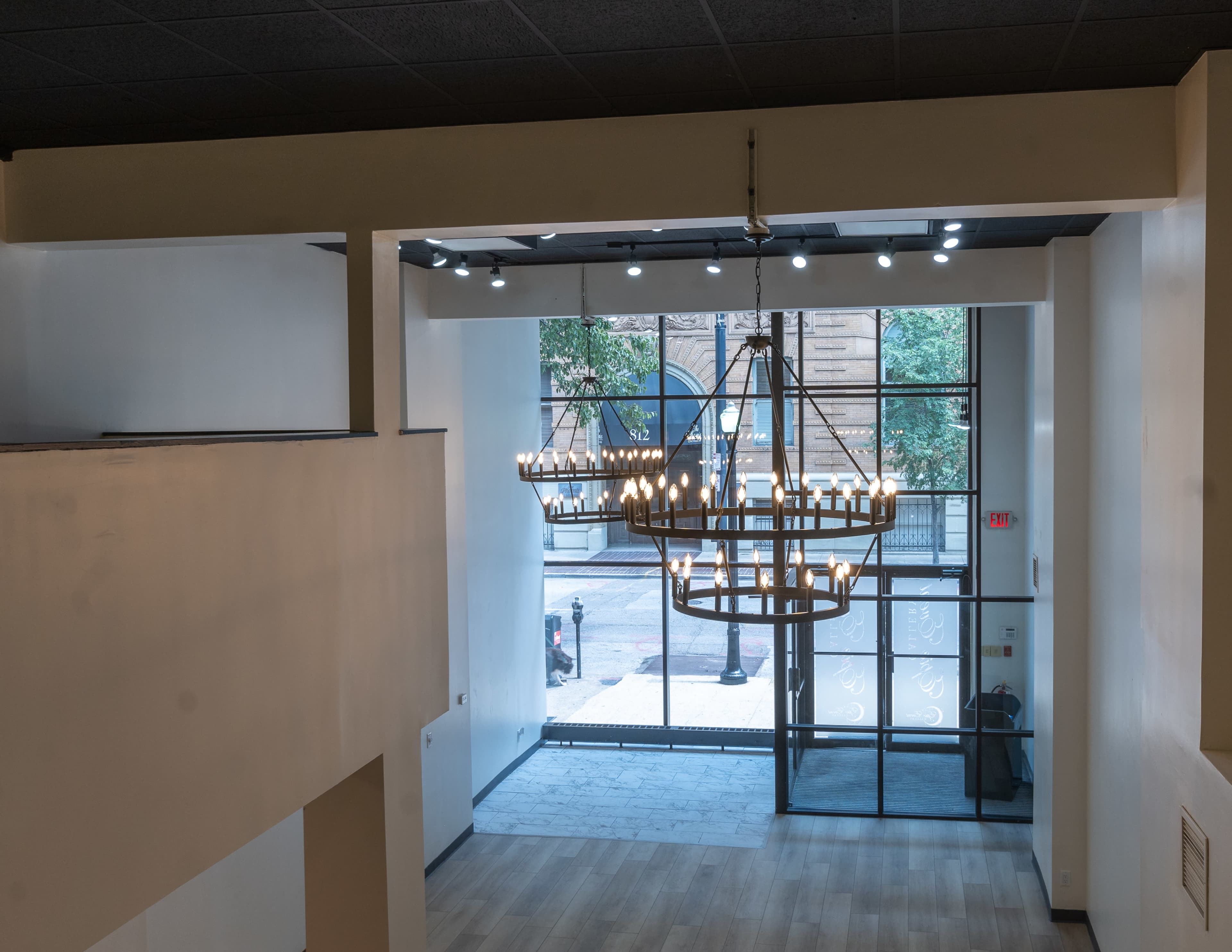 An interior space with a large chandelier hanging from the ceiling, illuminated by natural light coming through large windows.