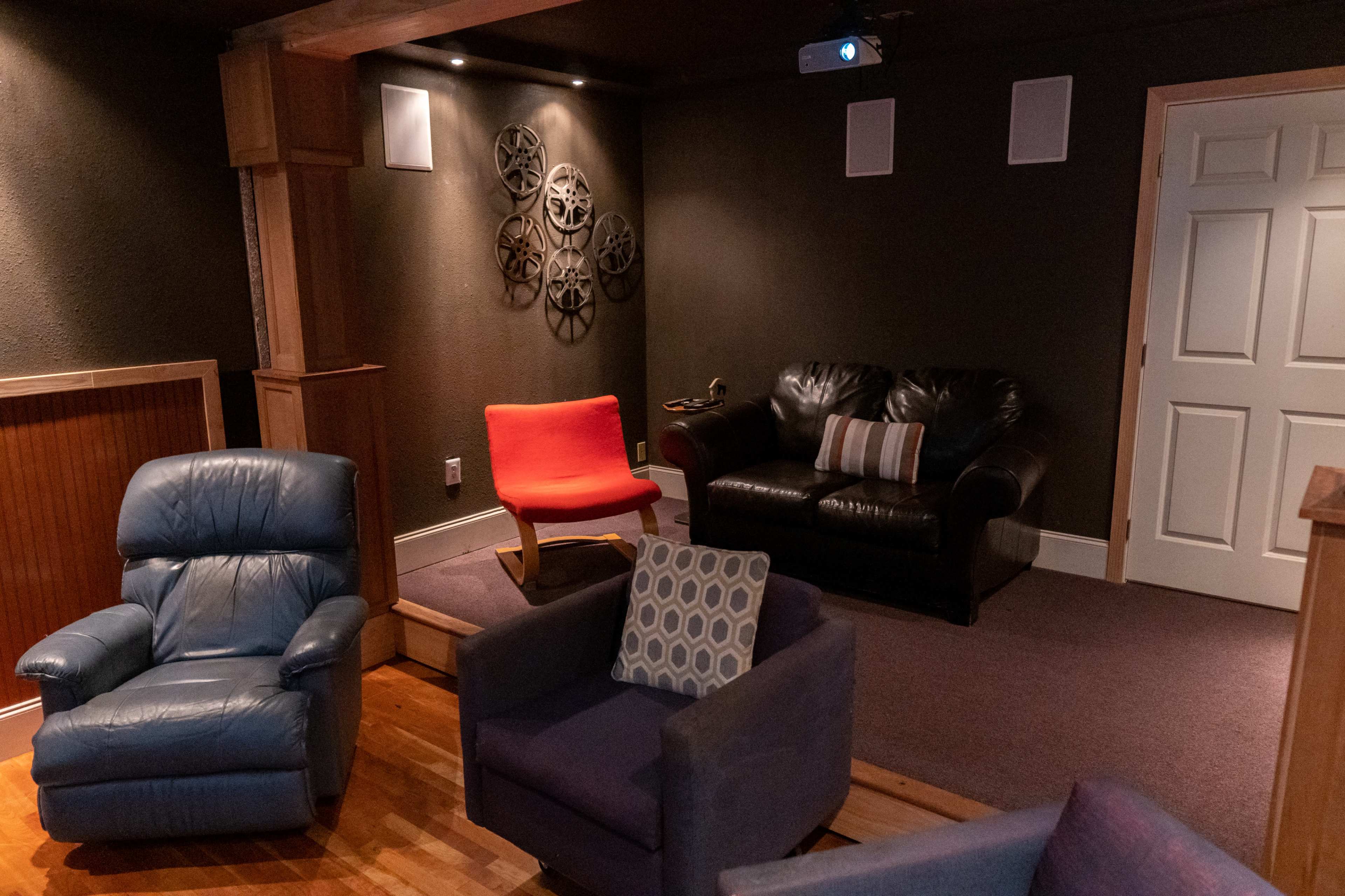 A cozy home theater area with various seating options, including blue and purple armchairs and a red accent chair, along with a projector and decorative film reels on the wall.