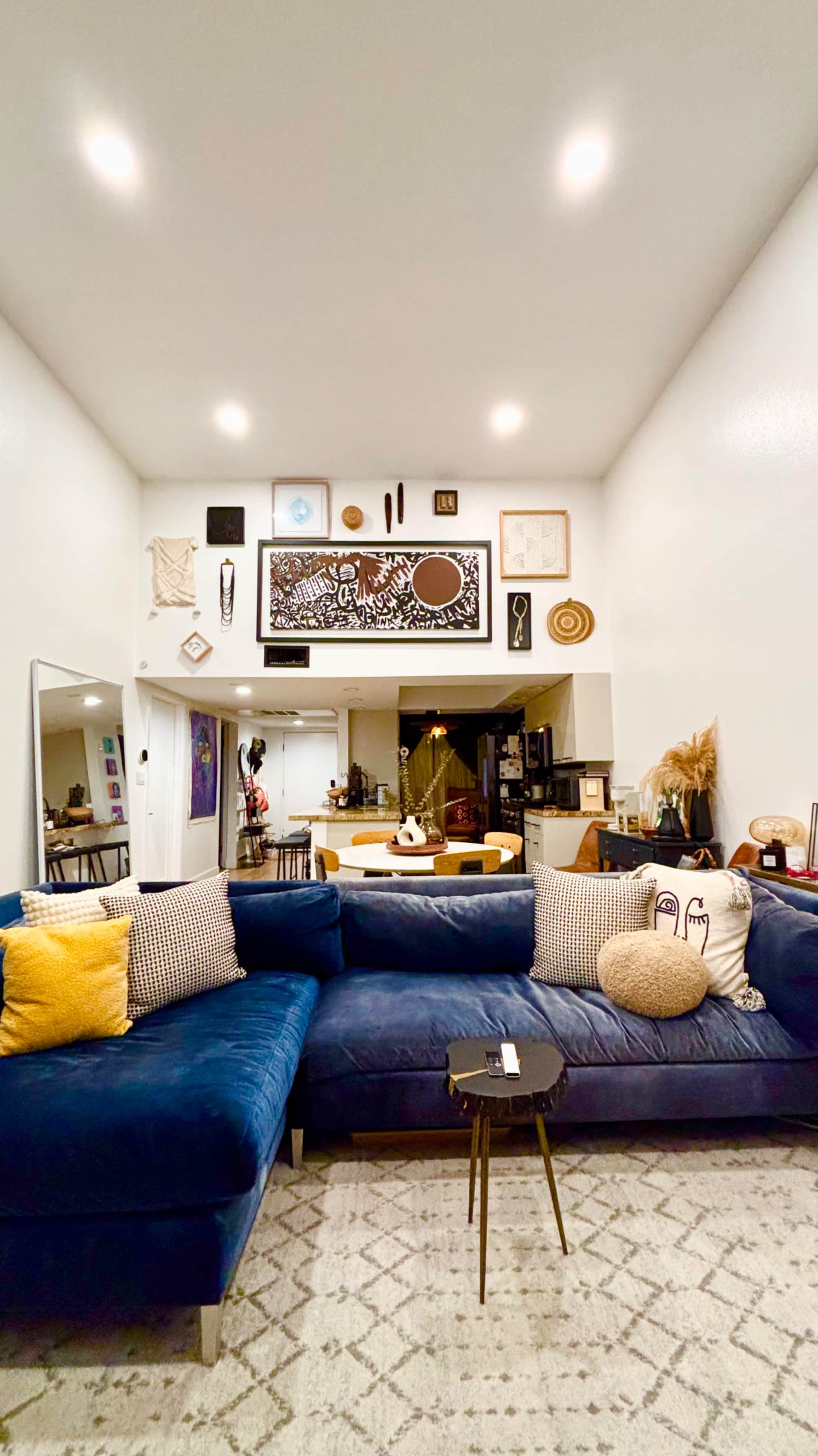 The image shows a modern living room featuring a blue sectional sofa with various decorative pillows, wall art, and a coffee table in front.