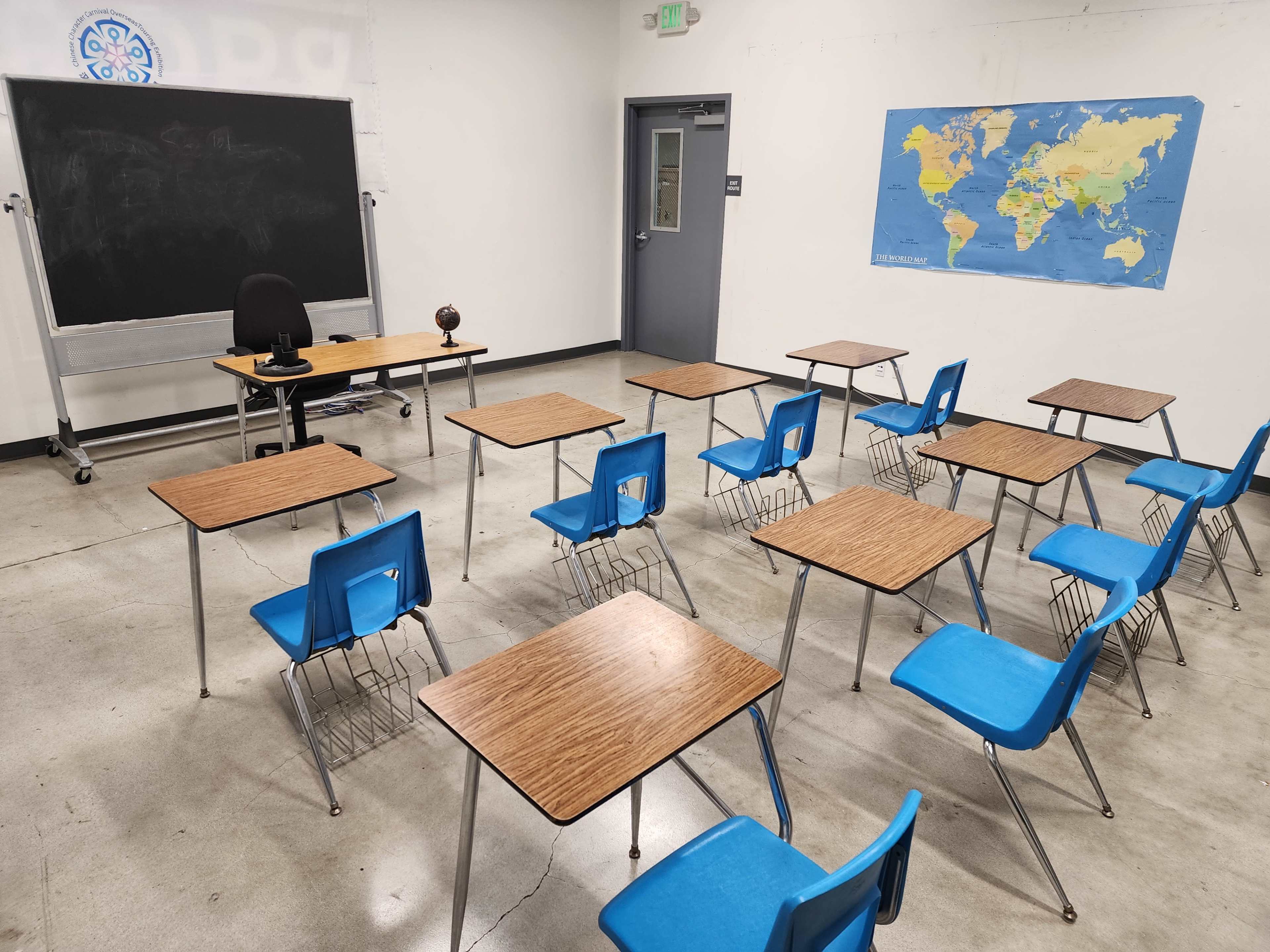 A classroom is arranged with multiple blue chairs and brown tables, featuring a globe and a map of the world on the wall.