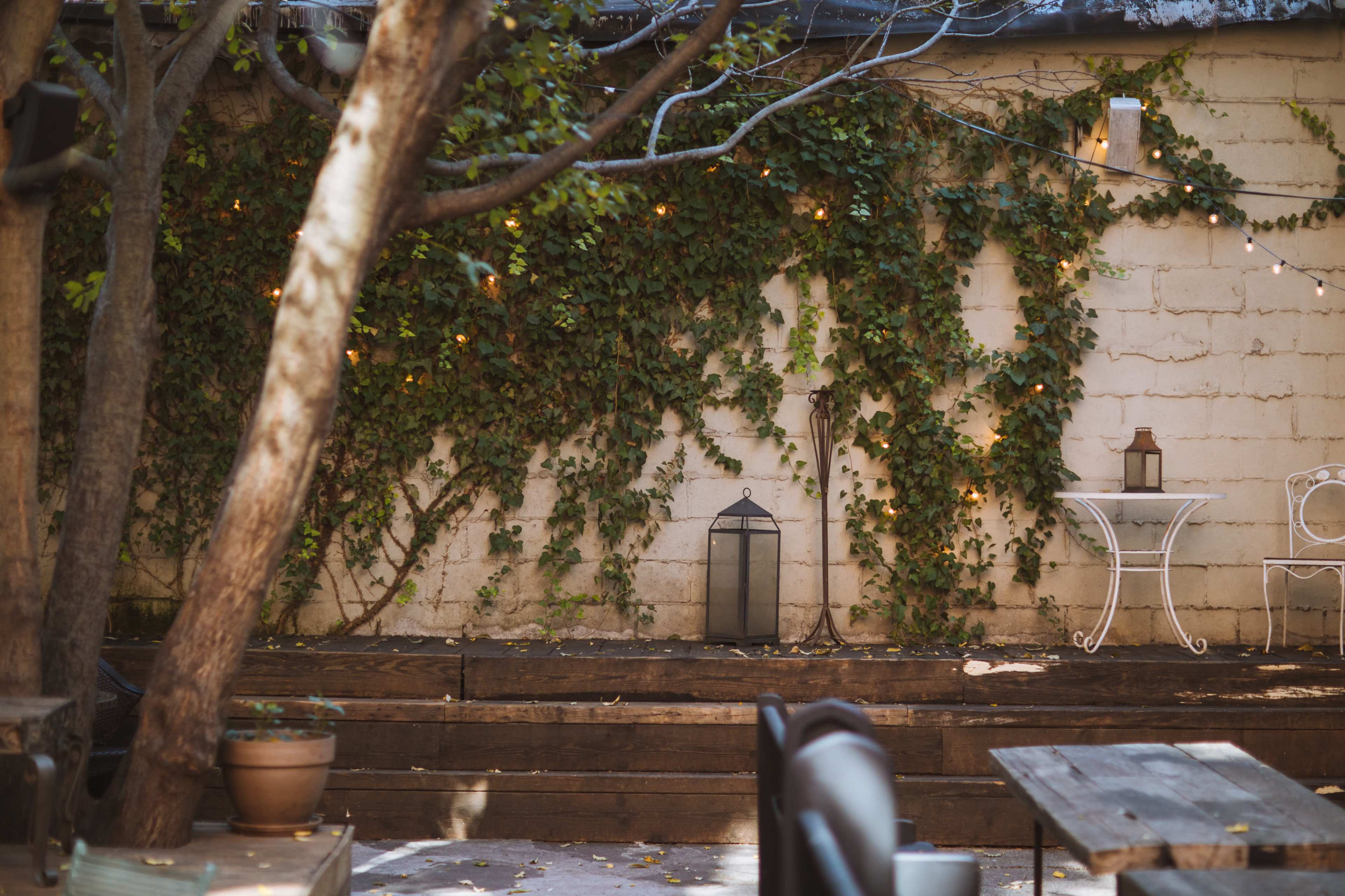 A garden area features wooden decking, a small white table with a chair, a lantern, and an ivy-covered stone wall.