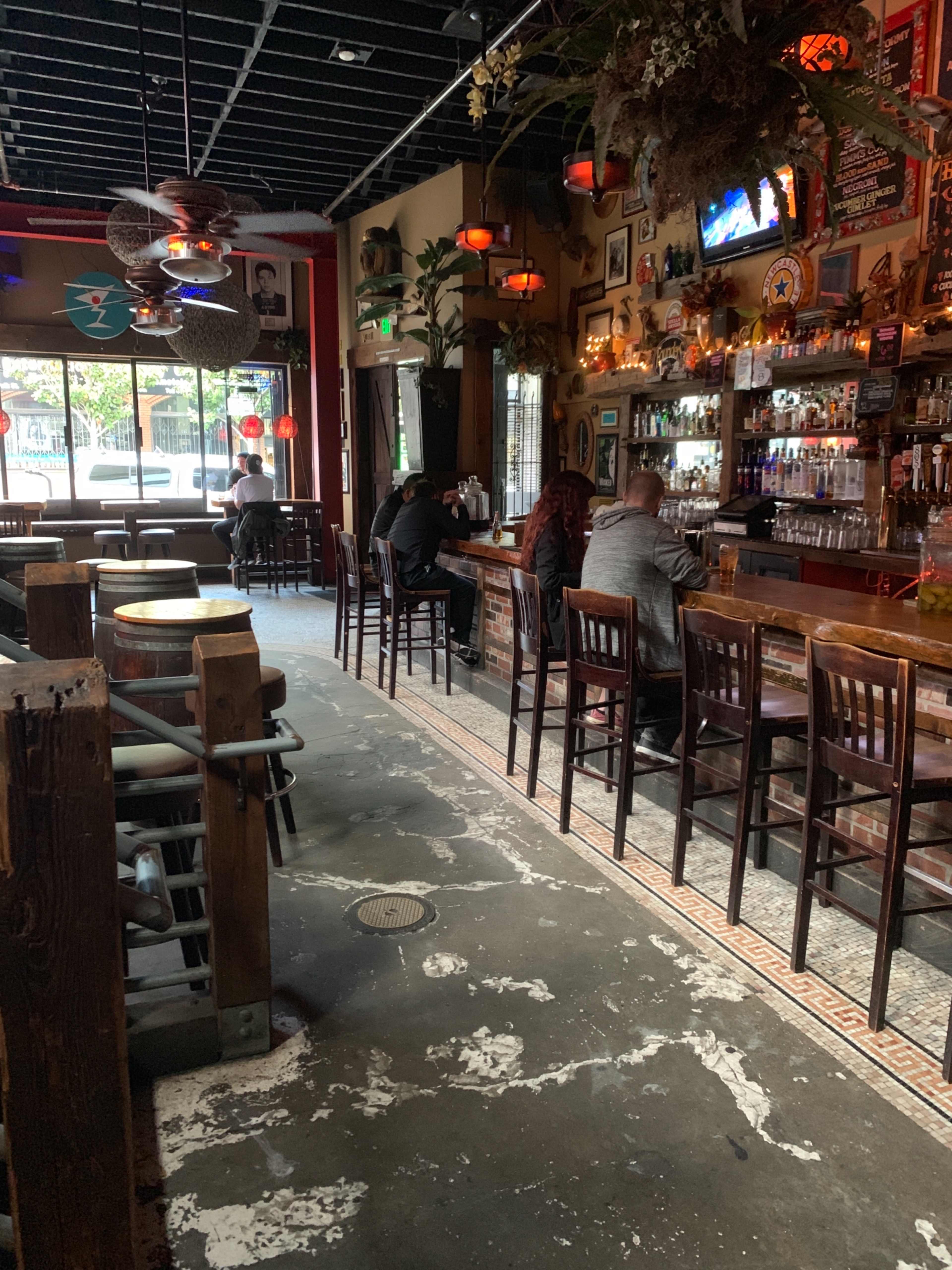 The image shows a dimly lit bar with a wooden counter, several patrons seated, and decorative elements on the walls and ceiling.