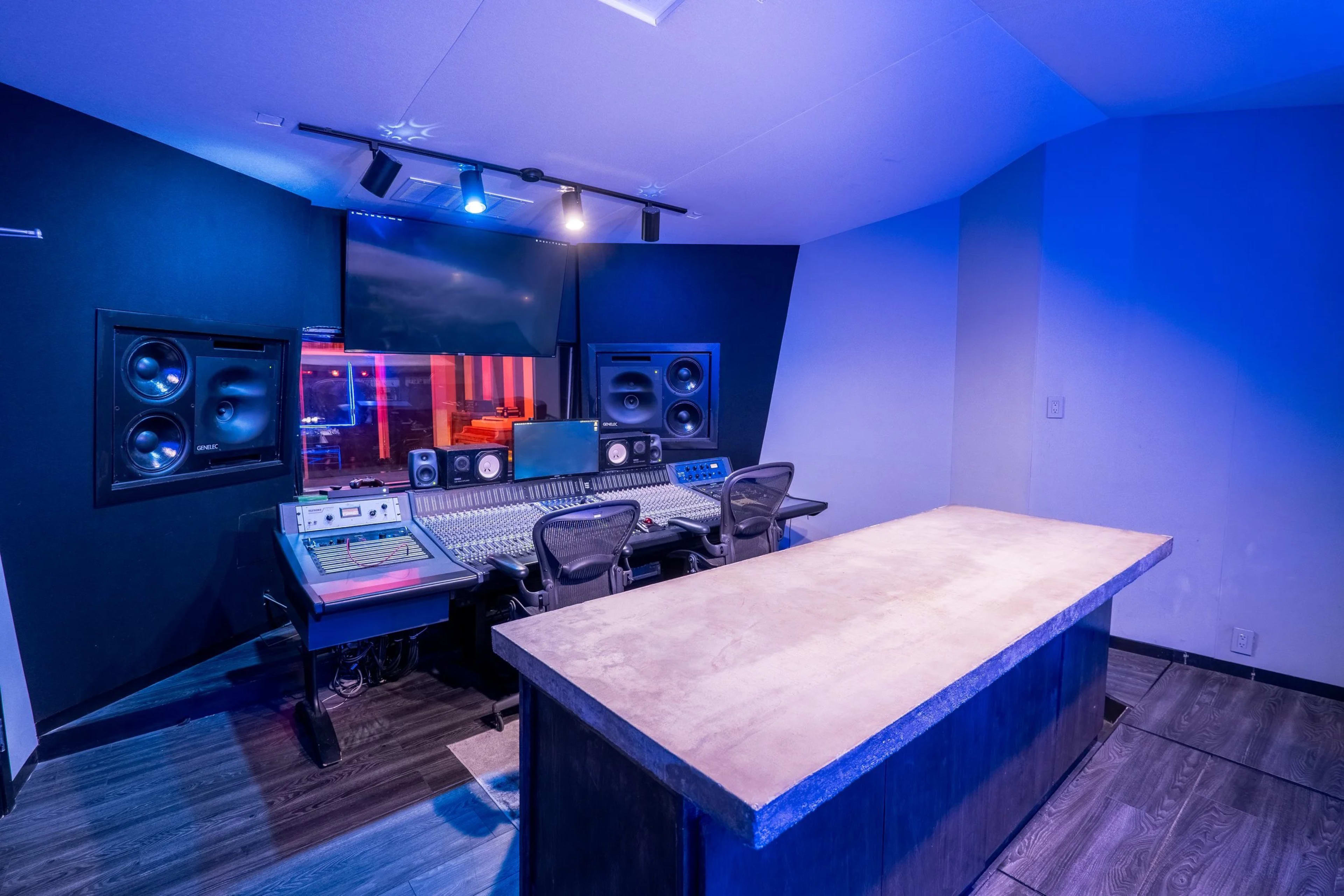 The image shows a modern music recording studio with a control desk, sound equipment, and a large screen, all set against a dark, ambient background.