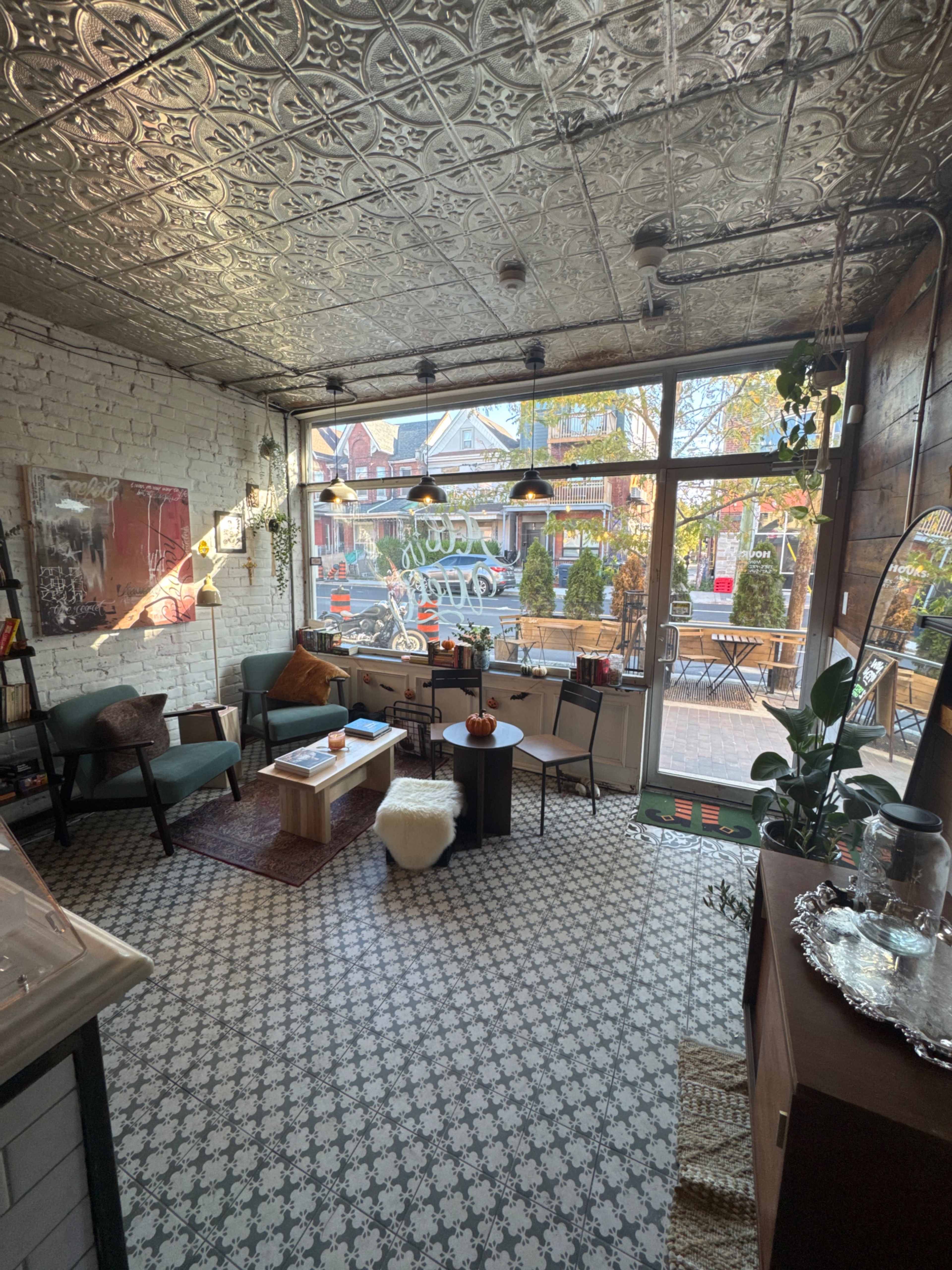 The image shows a cozy café interior with patterned tile flooring, a seating area with green chairs, and large windows allowing natural light to shine in.