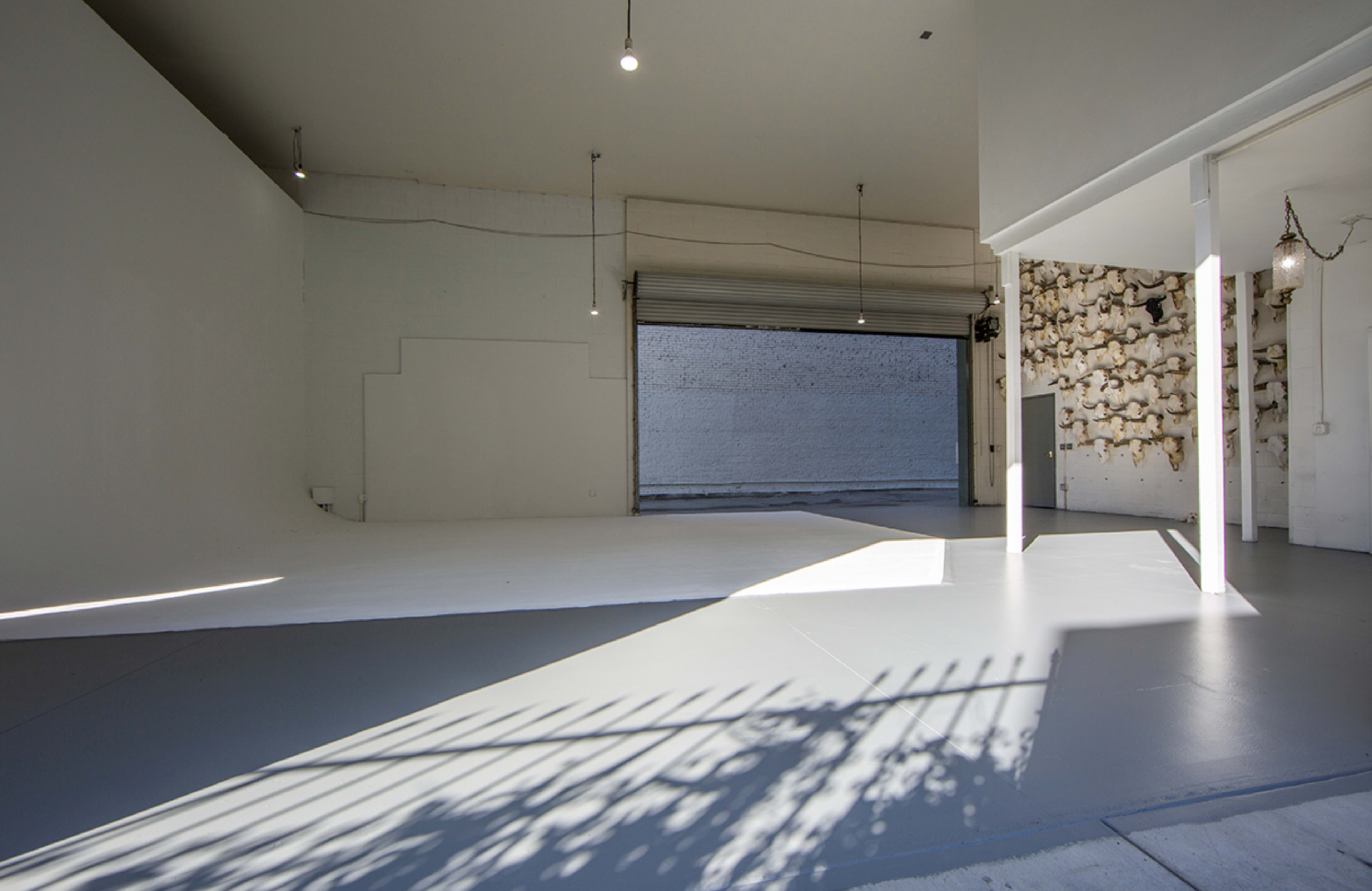 A spacious room features a gray floor, white walls, and a large opening that leads to an exterior area with a textured wall.