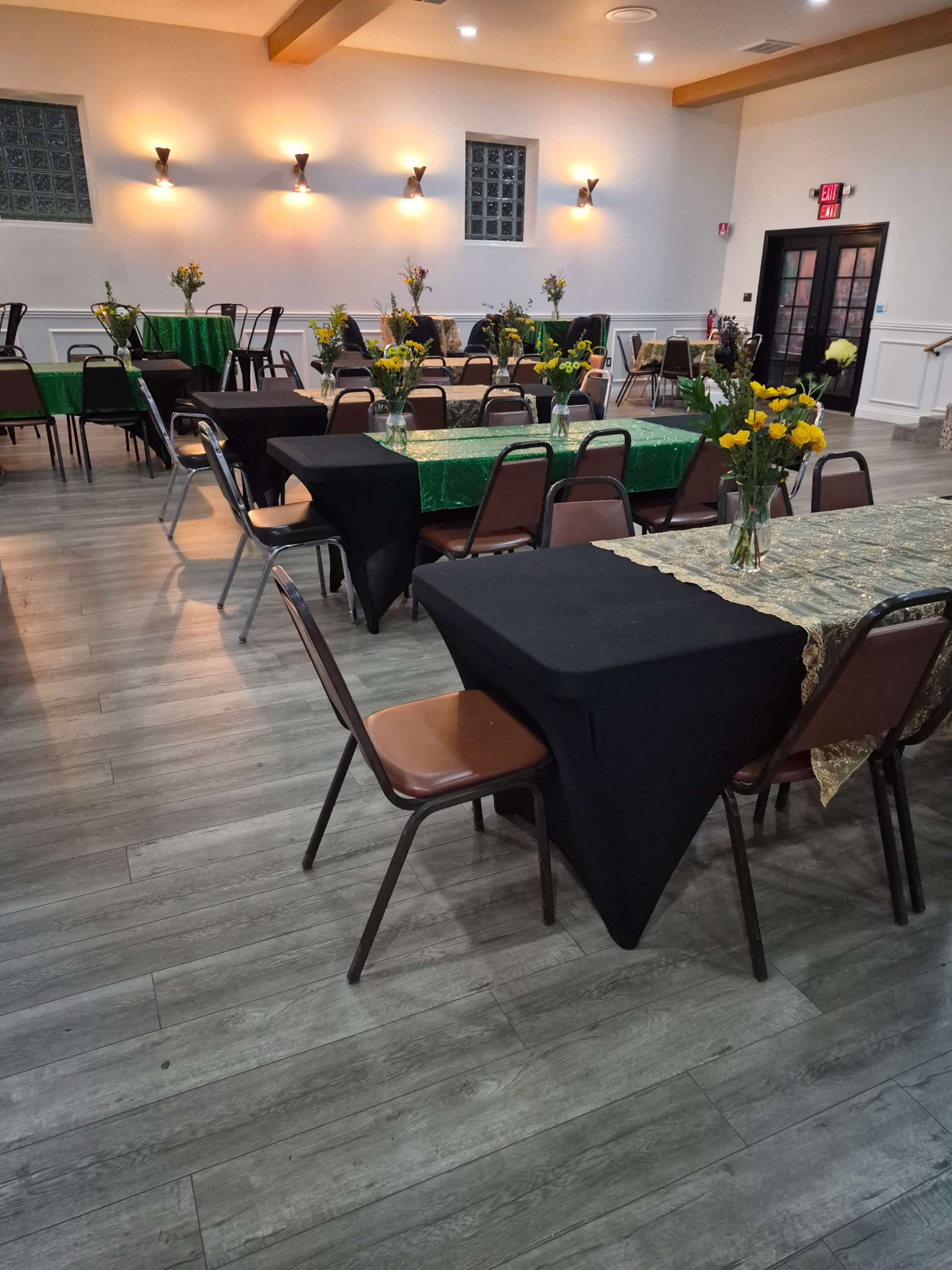 The image shows a banquet hall with multiple tables covered in black and green tablecloths, each adorned with floral arrangements.