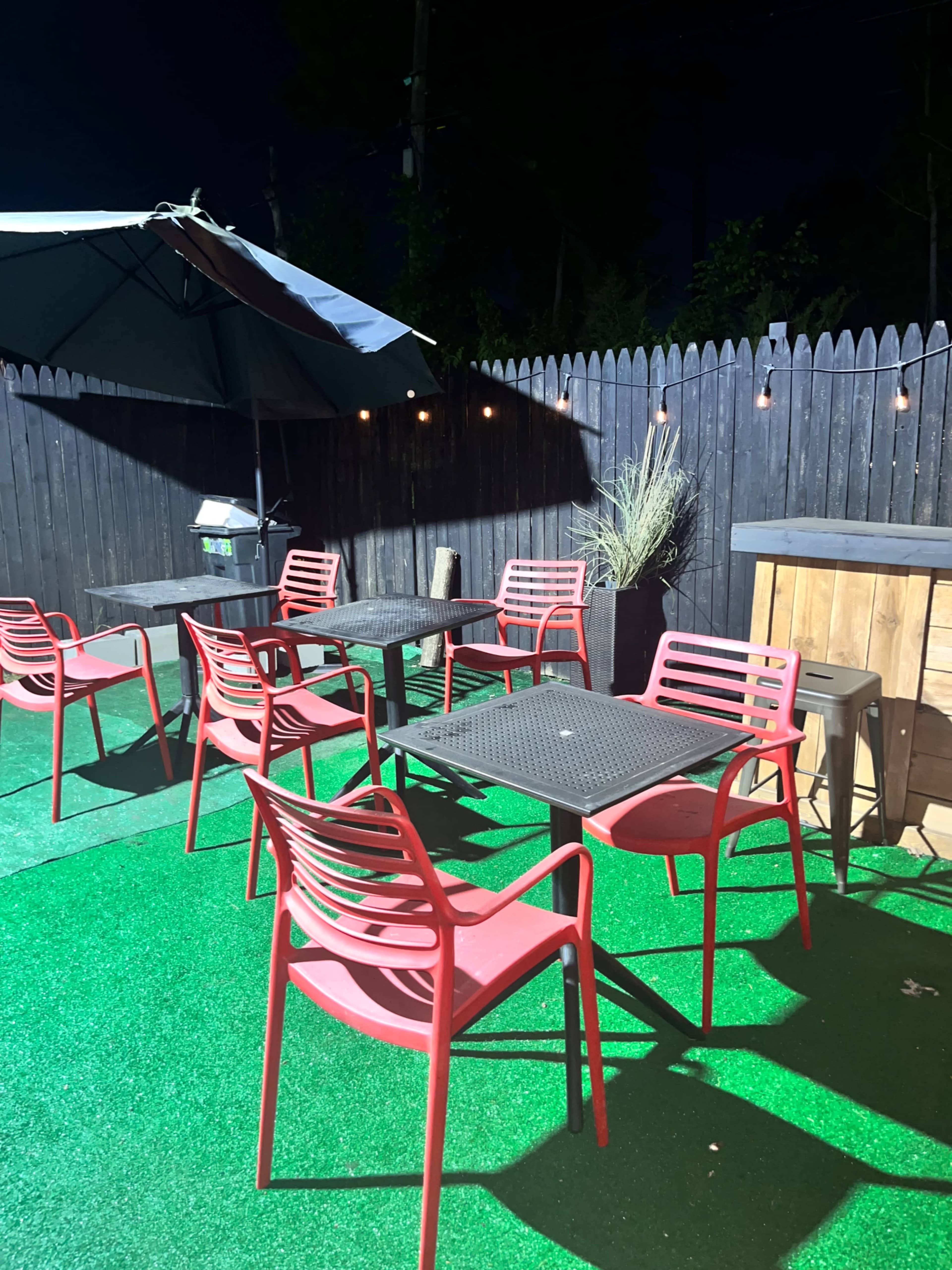 The scene features a patio area with red chairs and tables under a nighttime sky, surrounded by a wooden fence and string lights.