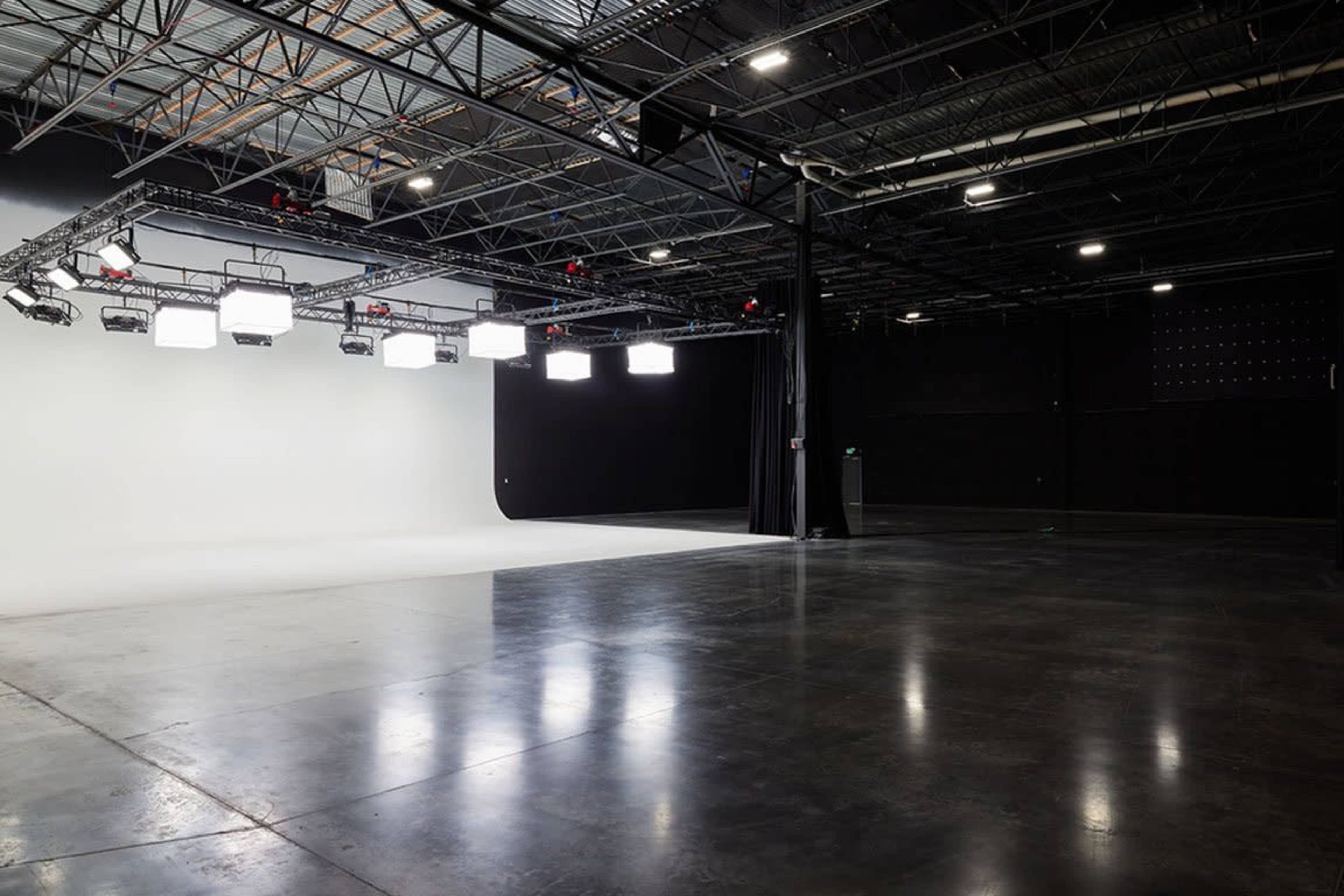 A spacious studio with a white backdrop on one side and black curtains on the other, illuminated by overhead lights.