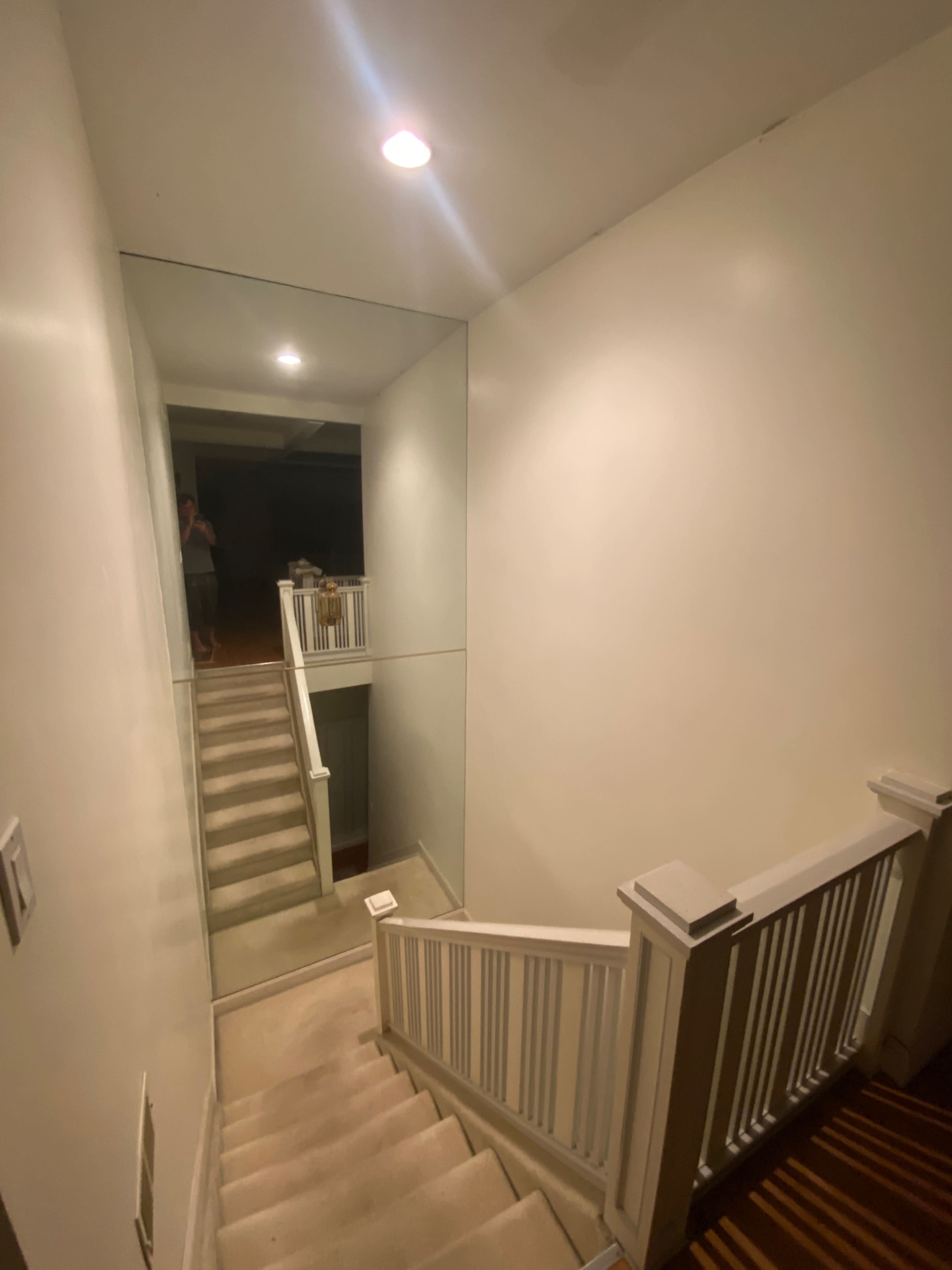 A staircase leads down to a lower level, with a large mirror on the wall and a light fixture overhead.