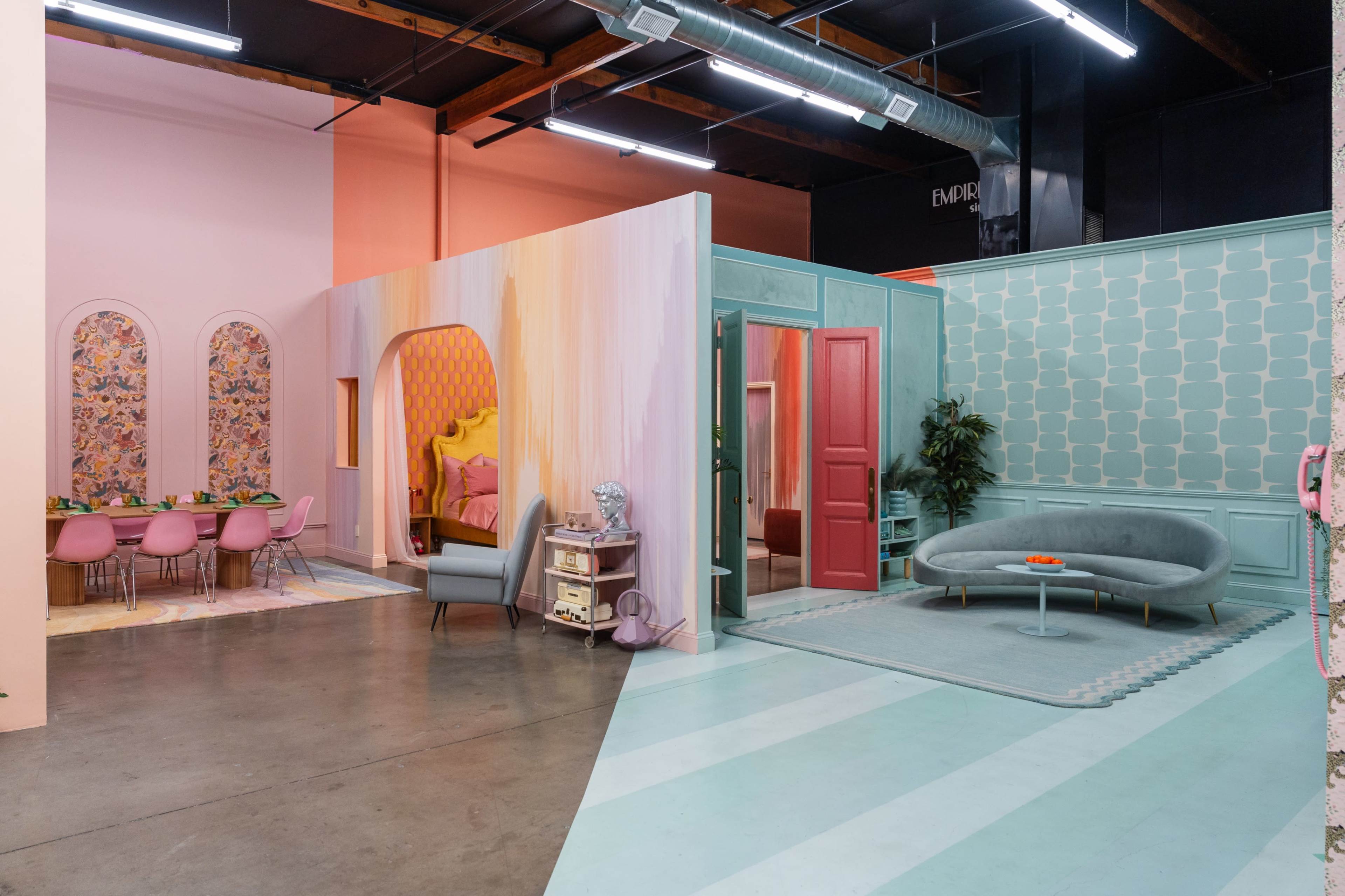 The image shows a modern interior space with vibrant pastel-colored walls, a dining area with pink chairs, and multiple rooms featuring unique design elements.