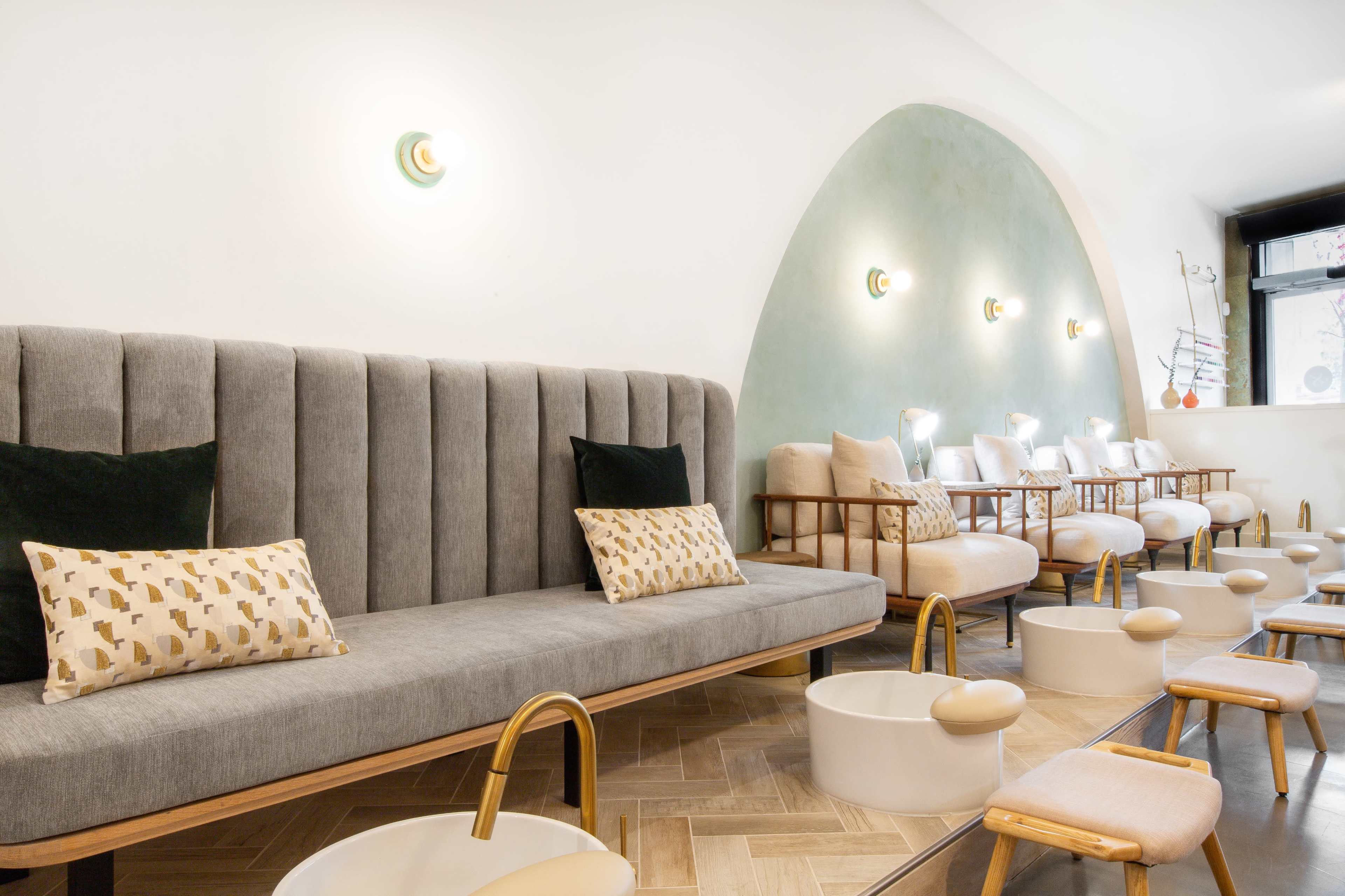 A modern interior space with a gray upholstered bench and several white chairs arranged along a wall, paired with small bowl-like structures on the floor.