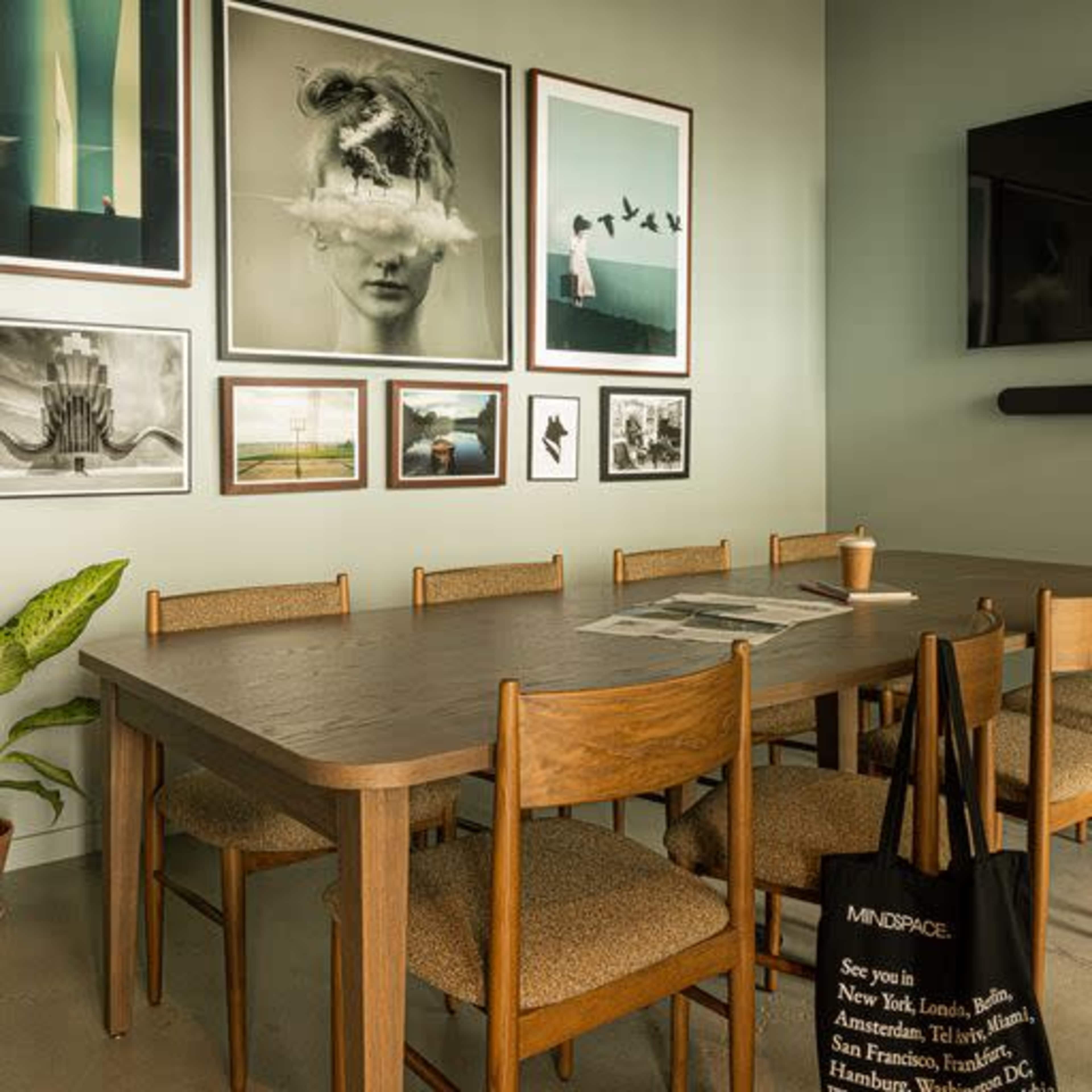 A dining area features a wooden table surrounded by chairs, with a gallery wall displaying various framed artworks.