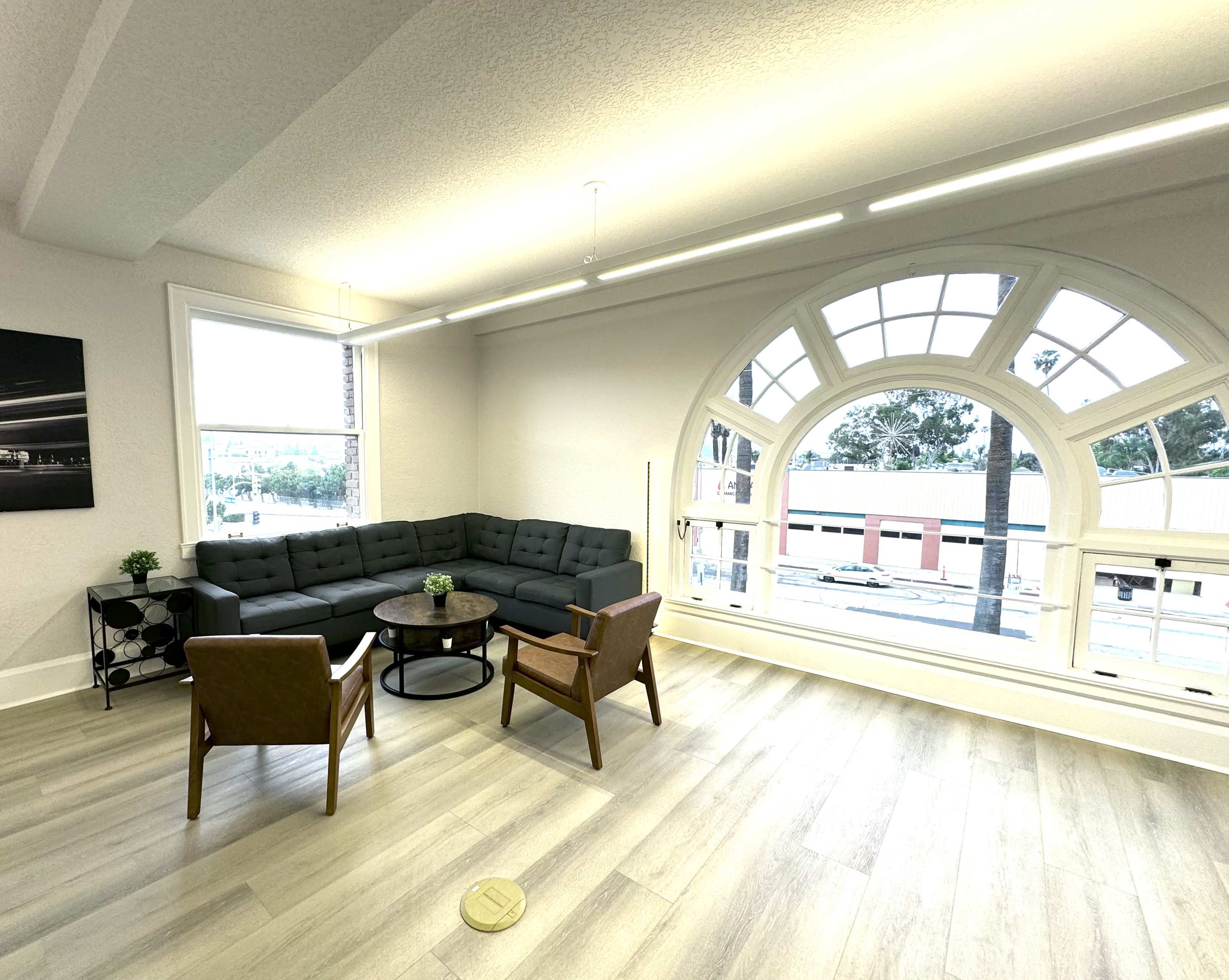 A modern living space featuring a gray sectional sofa, two brown armchairs, a small round coffee table, and large arched windows.