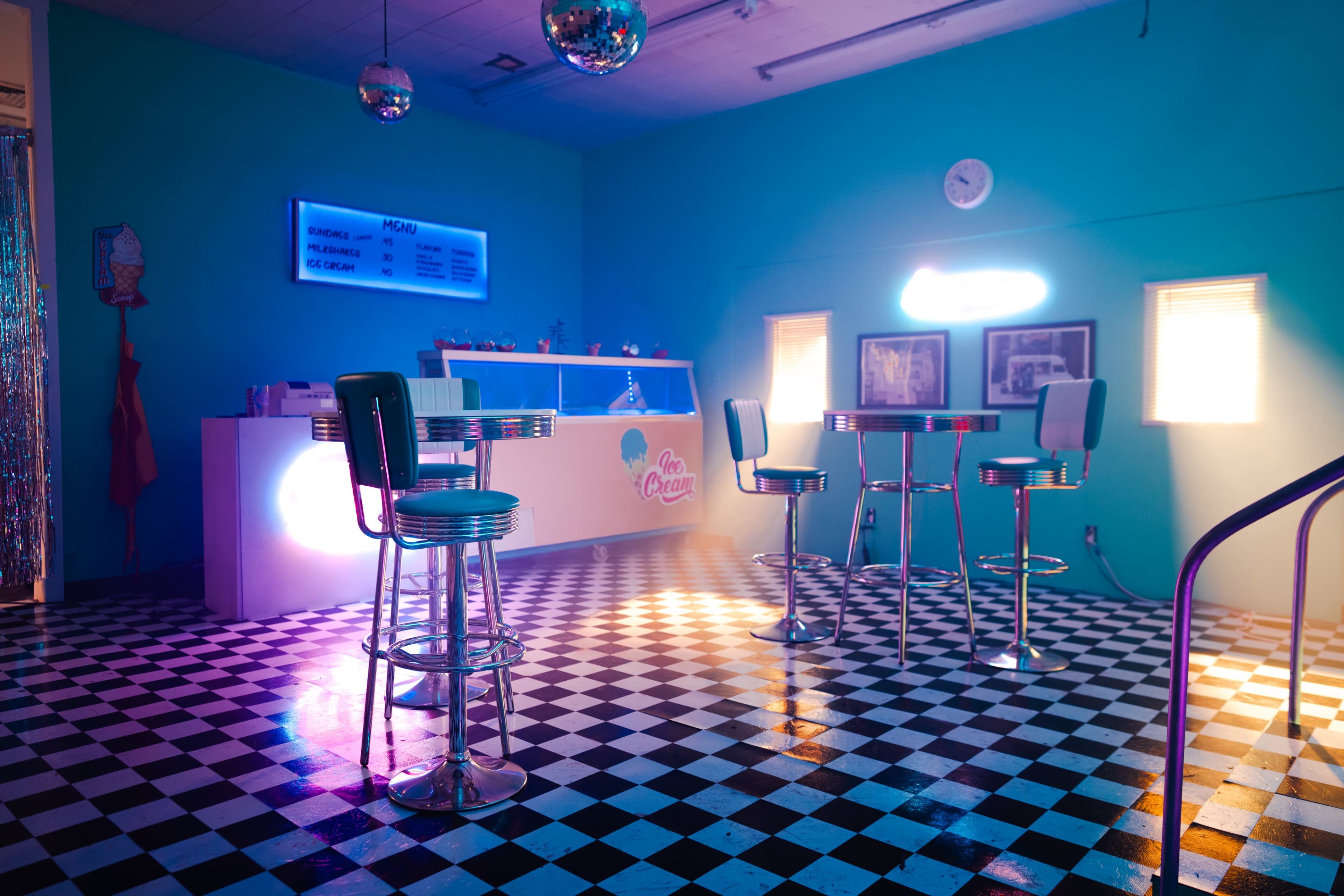 A retro-style ice cream shop with checkered flooring, chrome barstools, and colorful lighting.