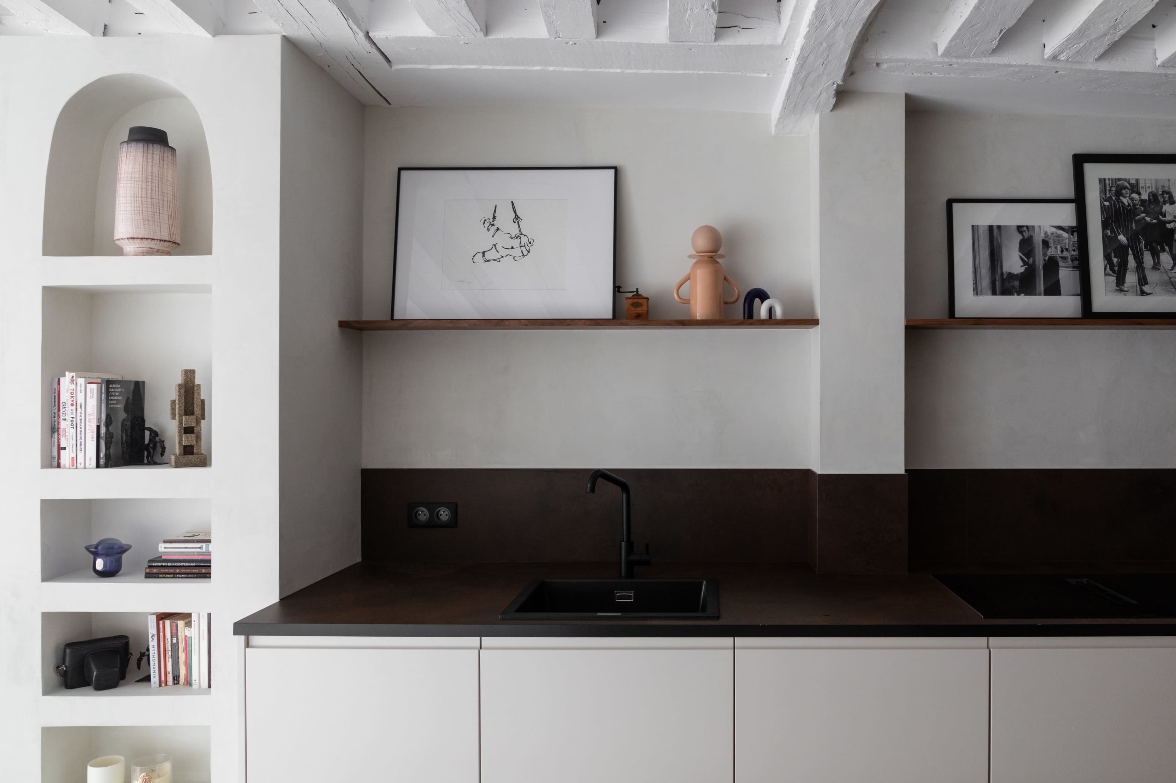 A modern kitchen features a dark countertop, a black sink, and open shelving with decorative items and books.