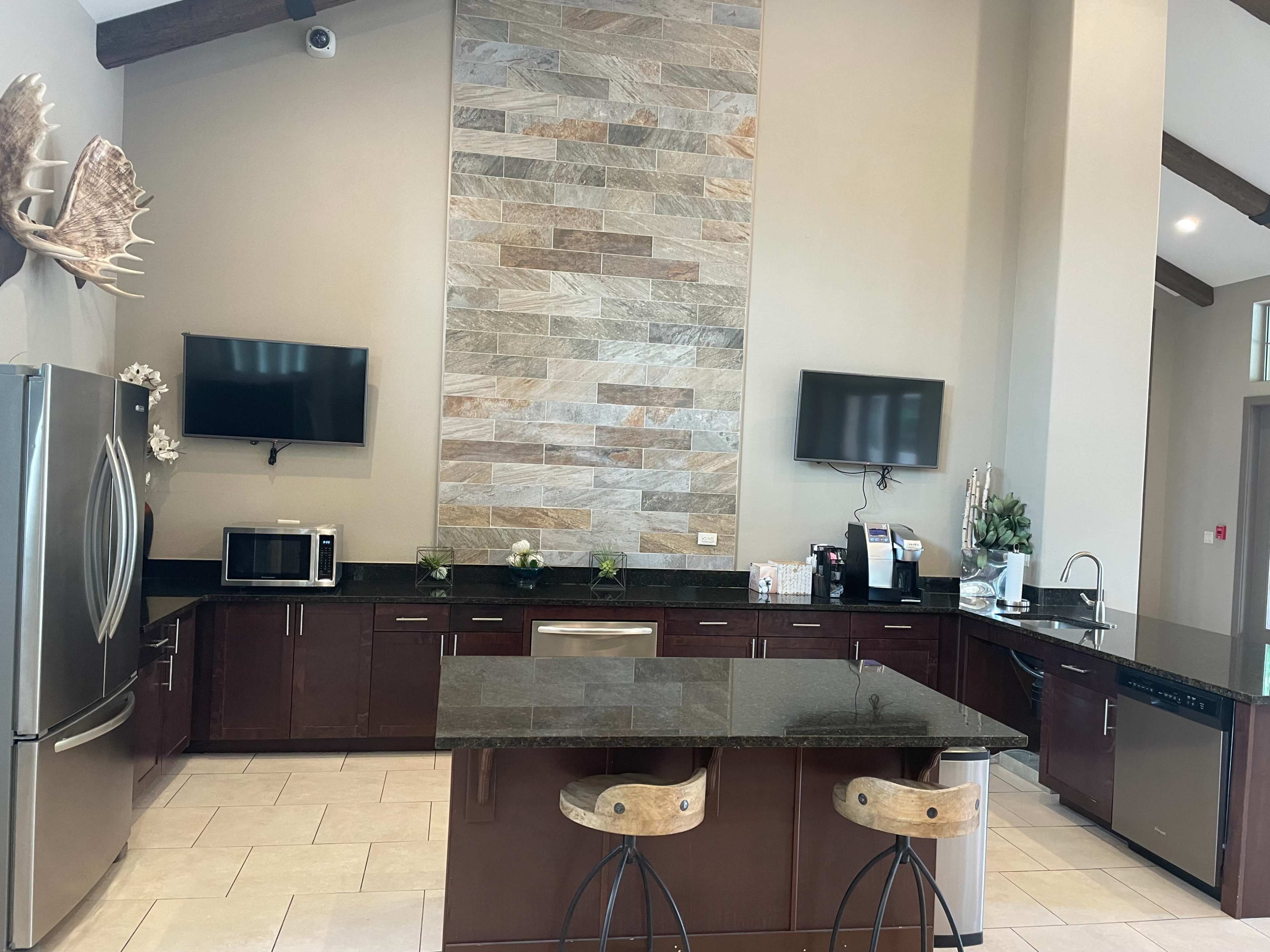 The kitchen features a large island with two stools, granite countertops, stainless steel appliances, and a stone accent wall.