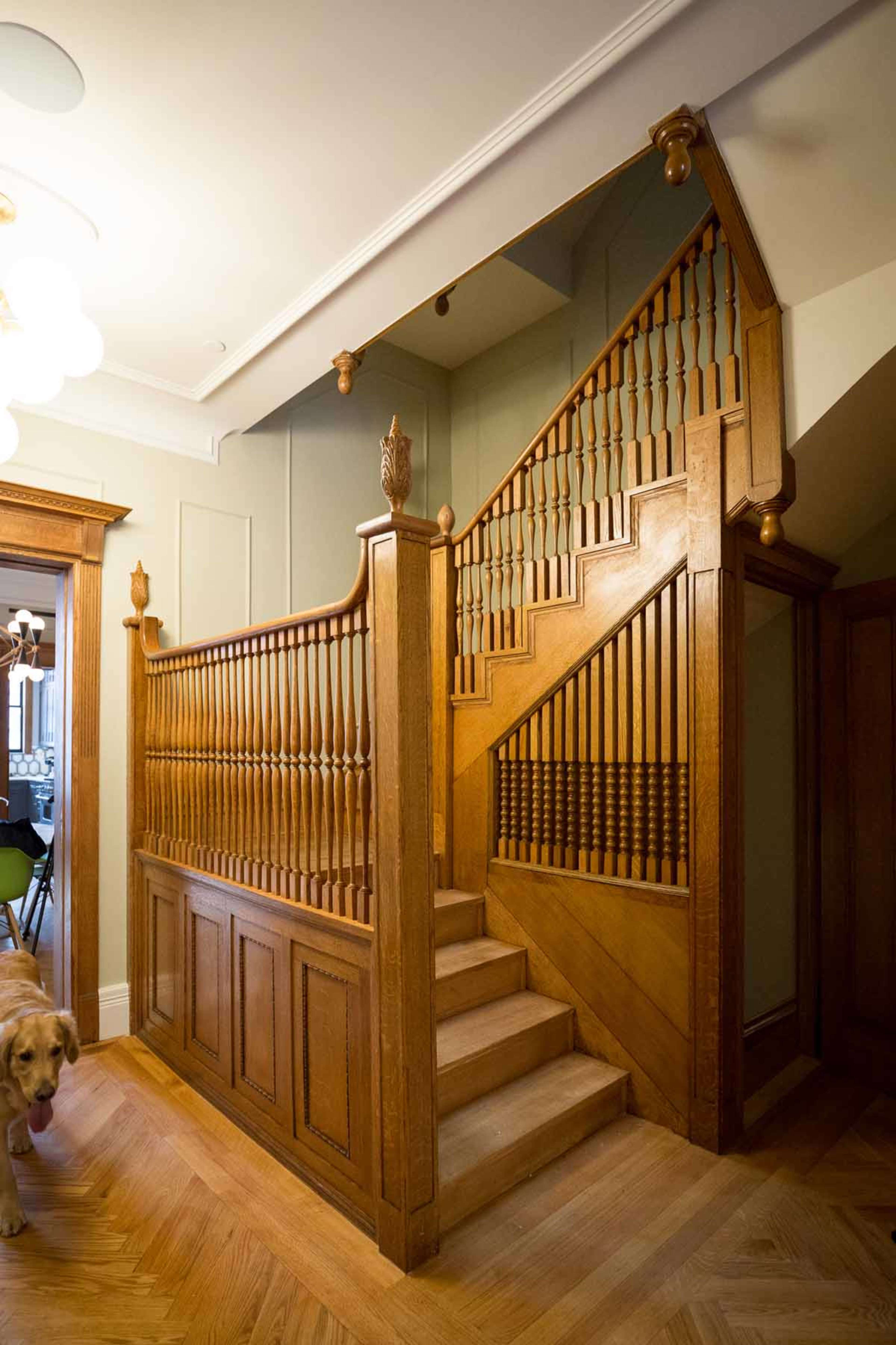 A wooden staircase with a detailed balustrade leads to a second floor in a well-lit entrance hall.