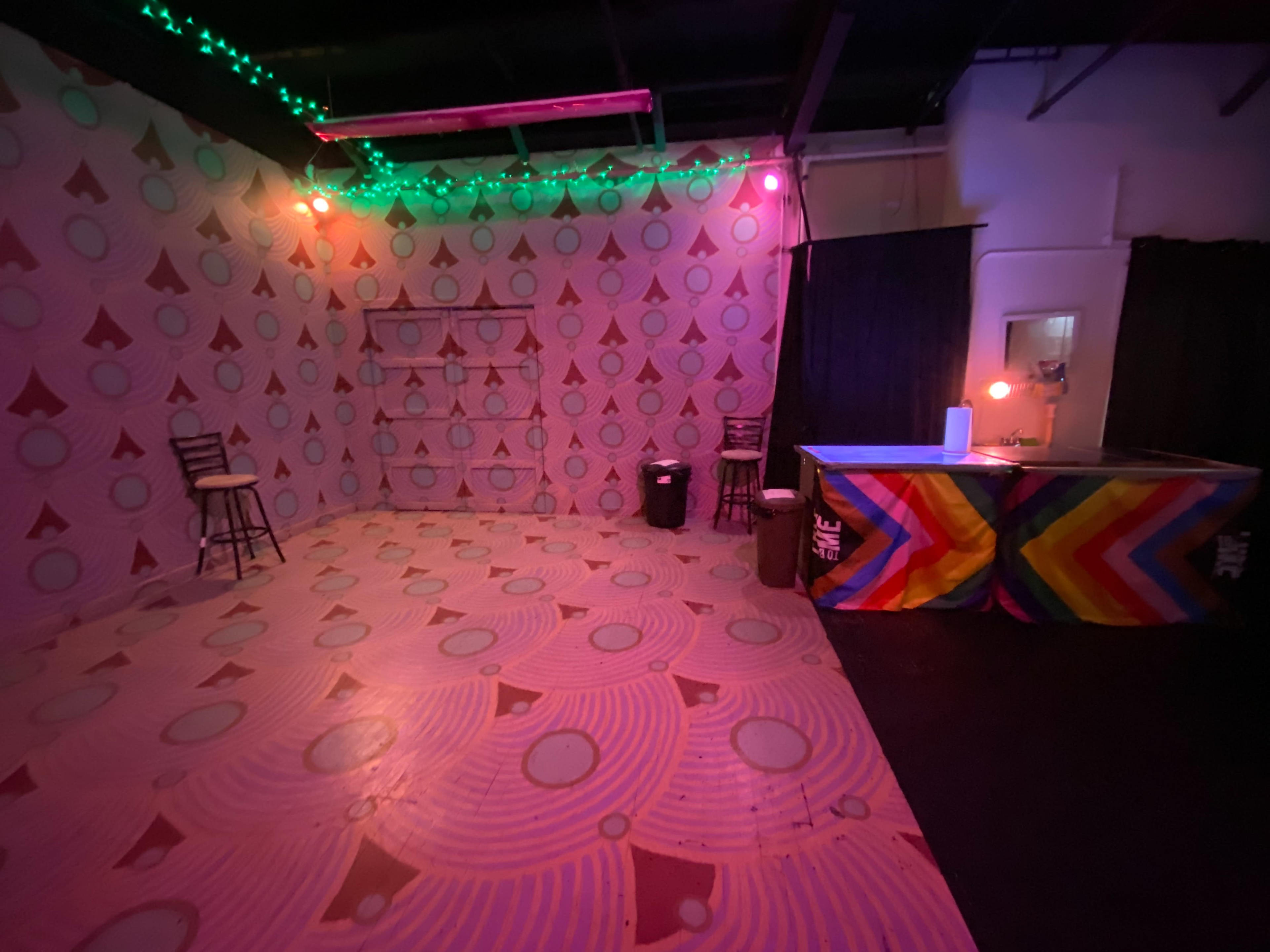 An indoor space with patterned walls, a bar with colorful decor, and two empty stools.