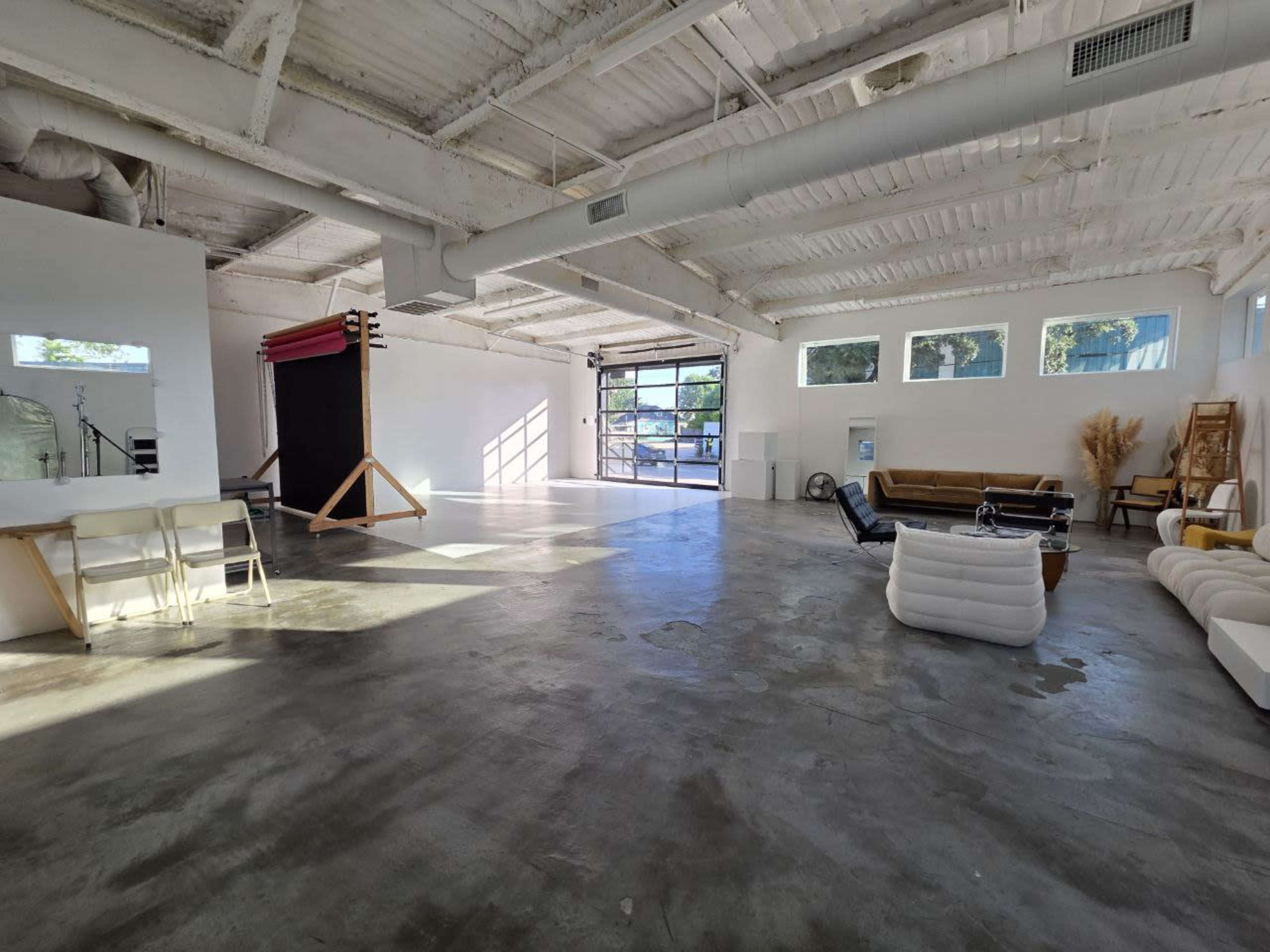 The image shows an industrial-style open space with polished concrete flooring, large windows, and various seating arrangements including a white couch and a brown sofa.