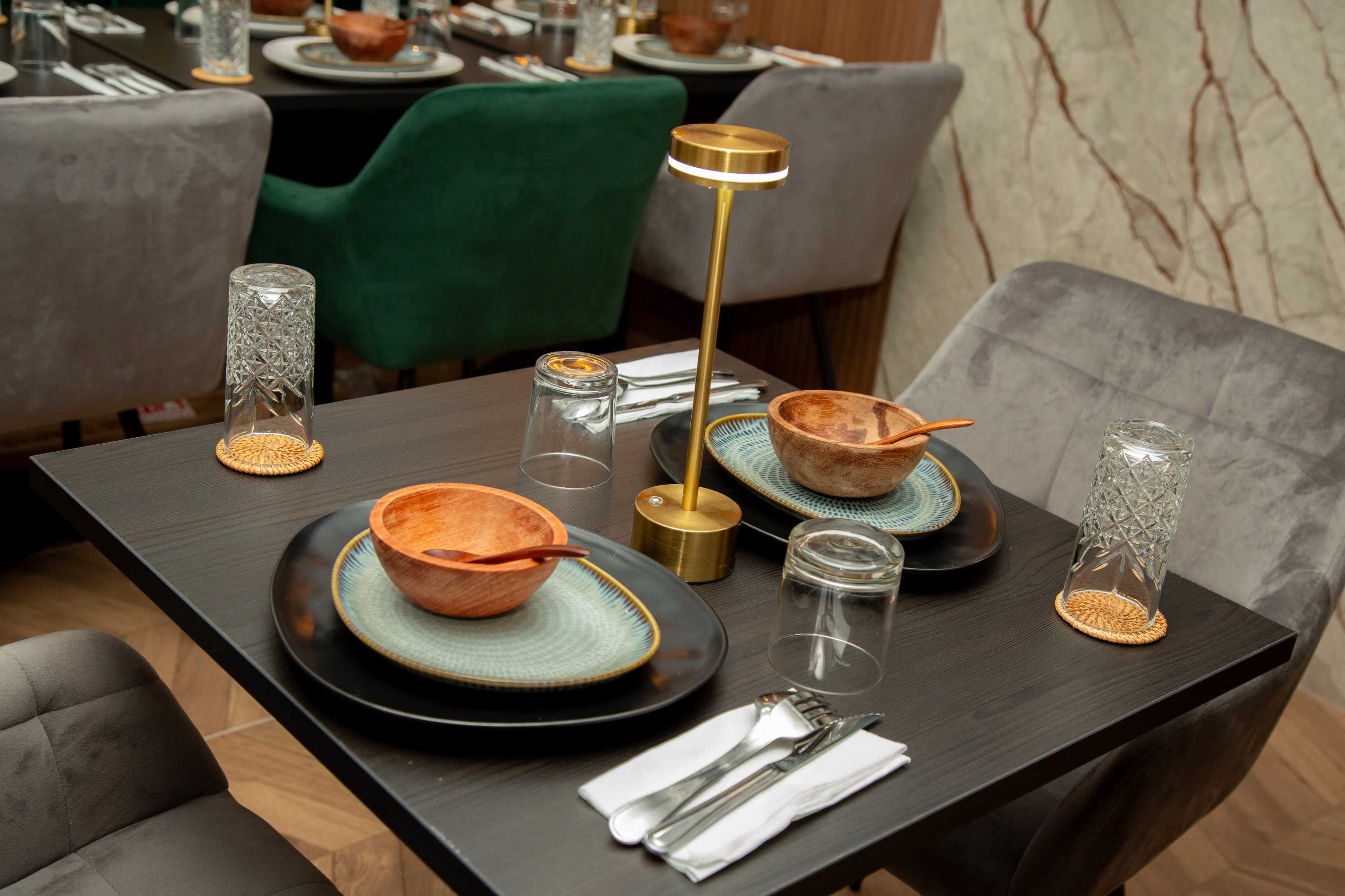 A dining table is set with two bowls, plates, glasses, and utensils in a modern restaurant.