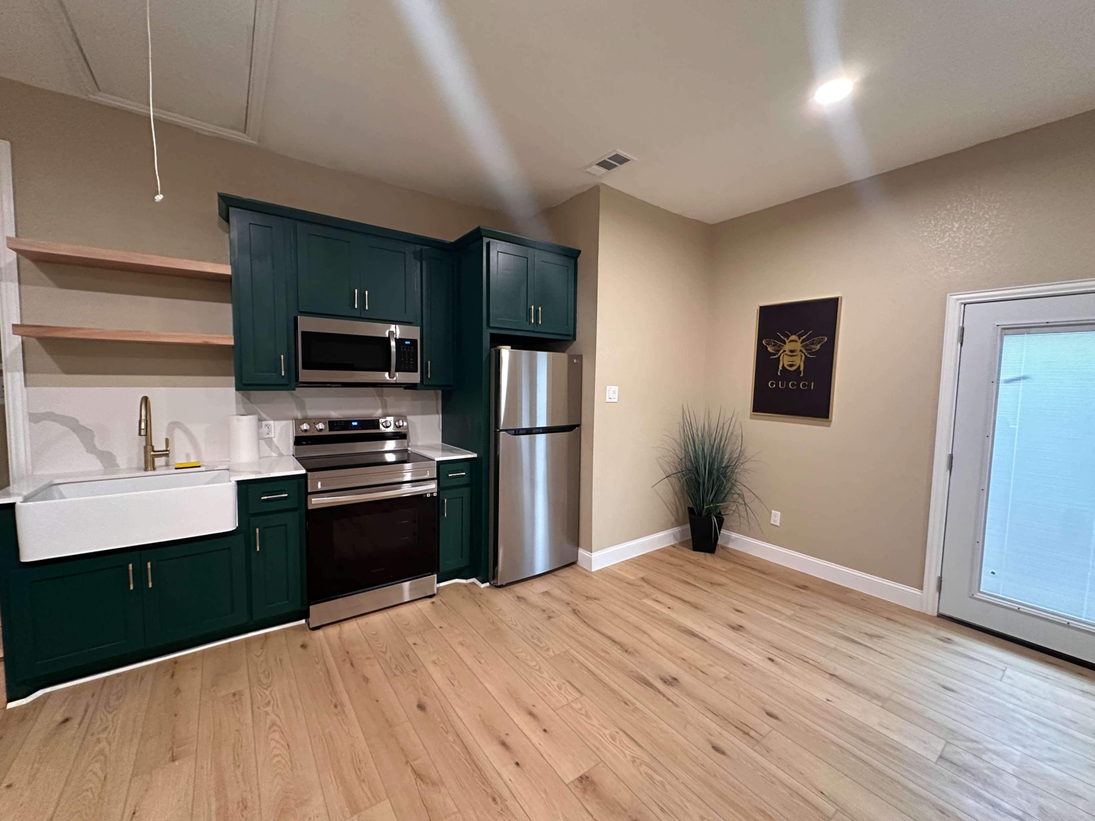 A modern kitchen with green cabinets, stainless steel appliances, a farmhouse sink, and a door leading to an outdoor area.