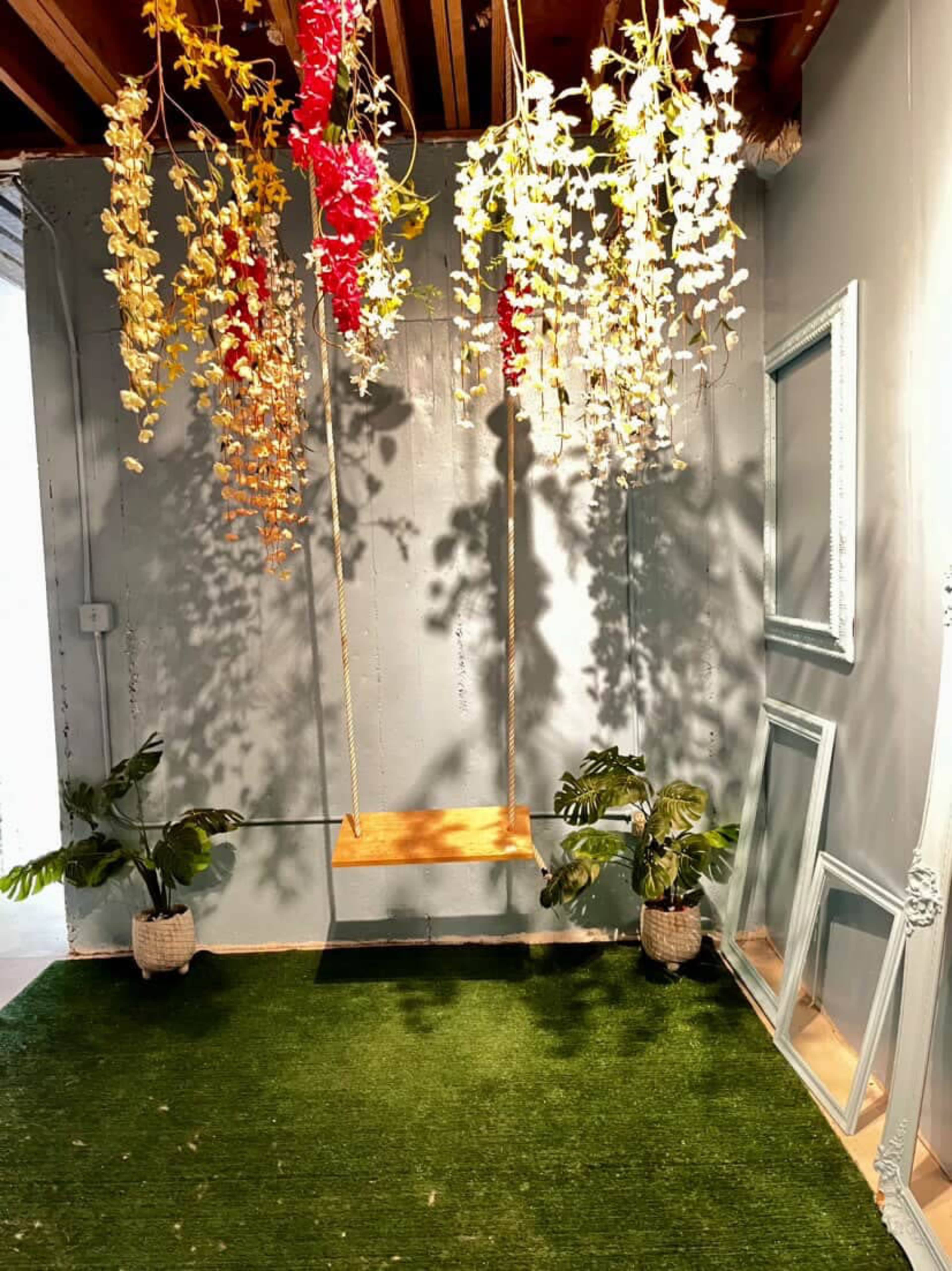 The image shows a decorative indoor space featuring a swing suspended from the ceiling, surrounded by hanging faux plants, and an area with artificial grass.