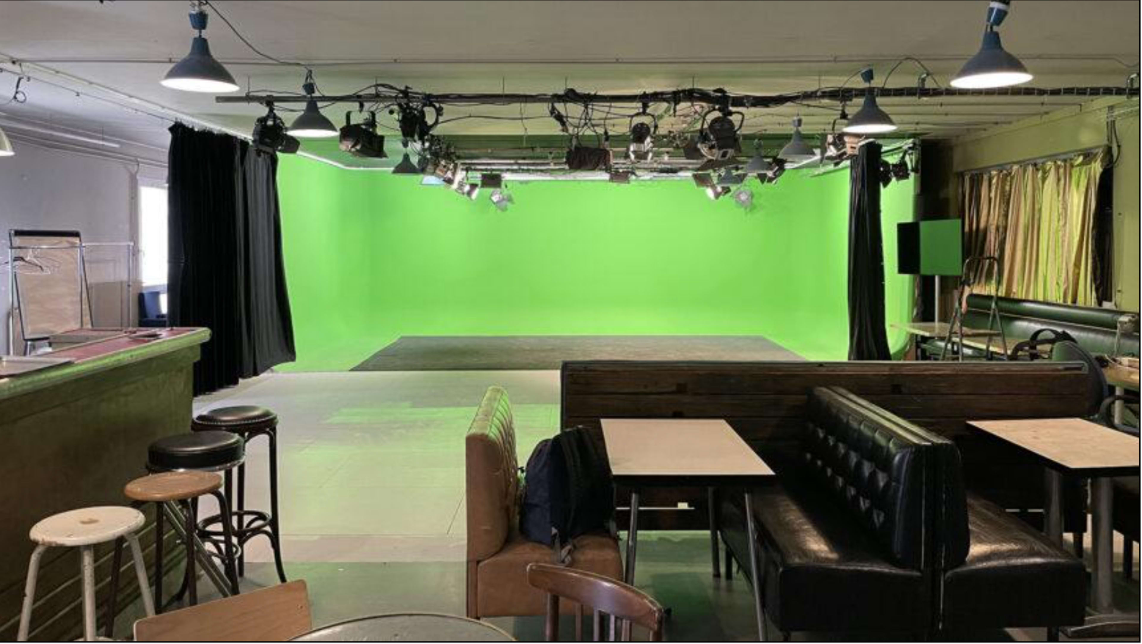 A studio space with a green screen backdrop, surrounded by various seating arrangements and lighting fixtures.