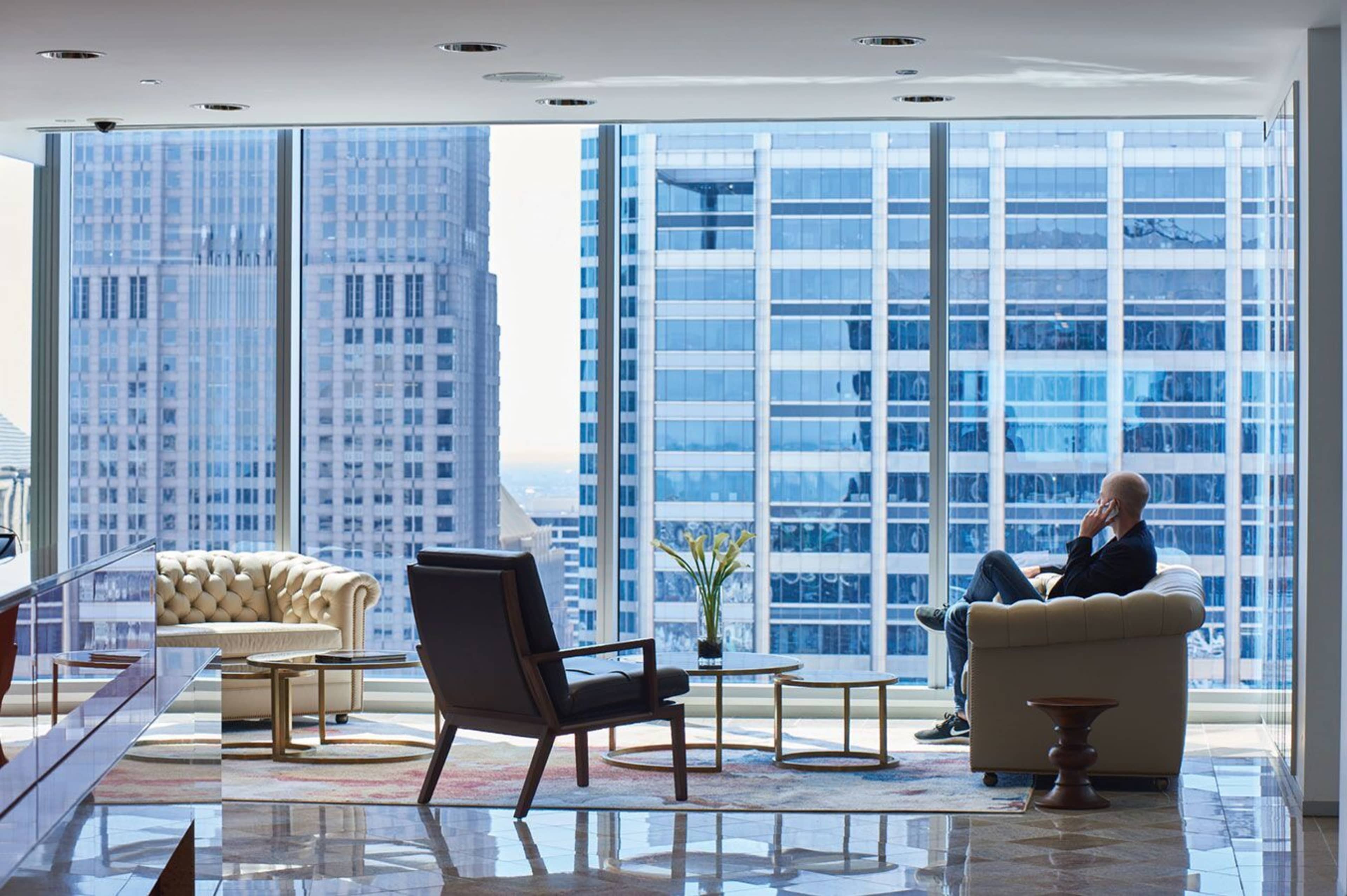 A man sits in a modern office lounge area with large windows overlooking a cityscape.