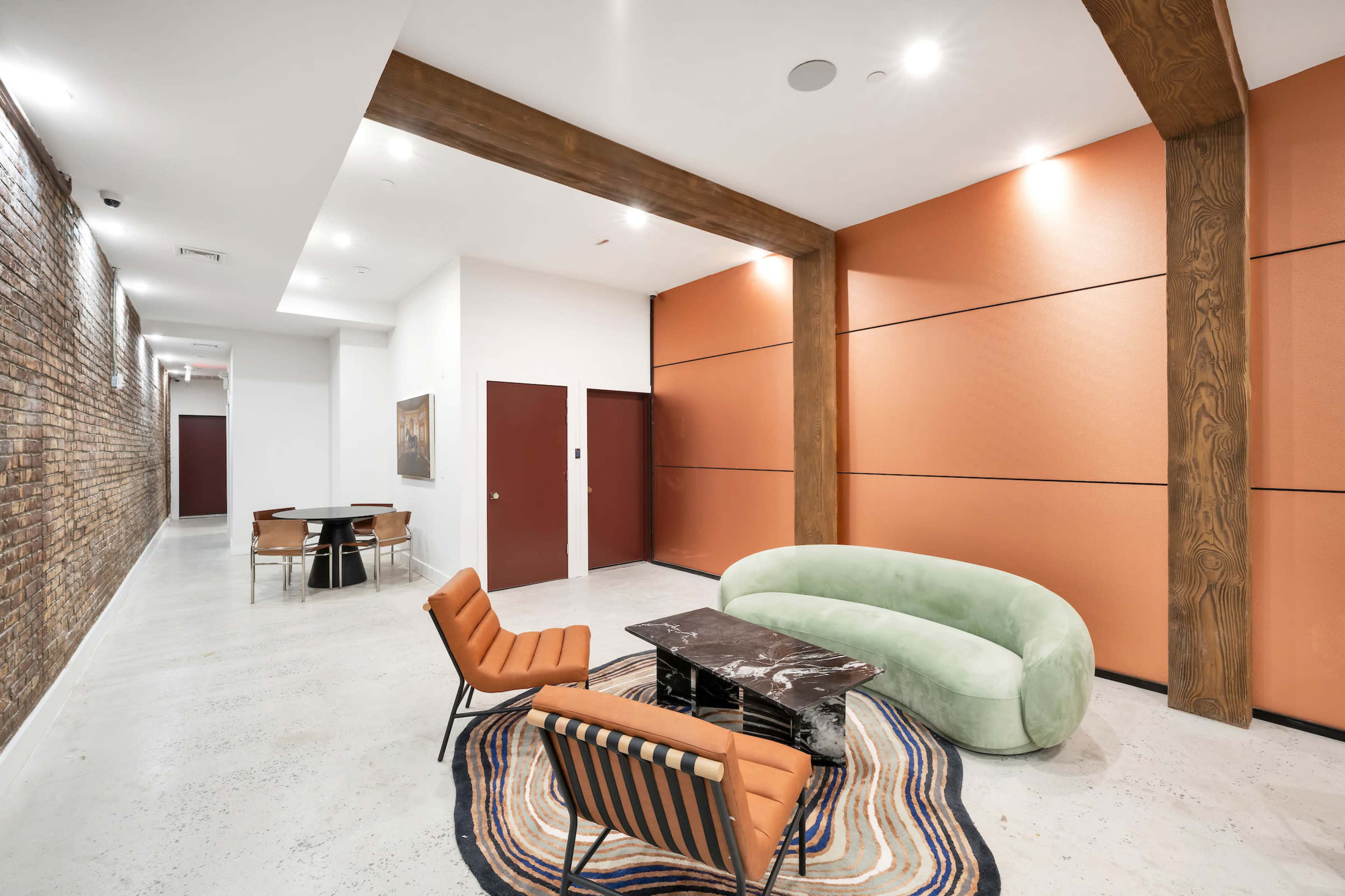 The image shows a modern indoor space featuring a green sofa, orange accent walls, and a patterned rug, with seating arrangements including striped chairs and a dining table.
