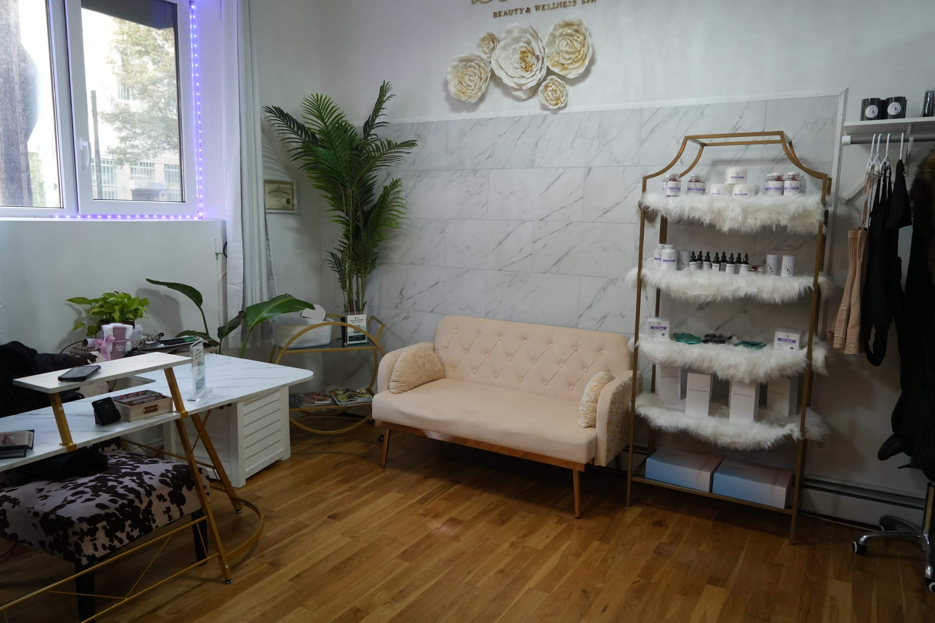 A cozy wellness space featuring a light-colored couch, a small table, a shelf with skincare products, and a decorative plant.