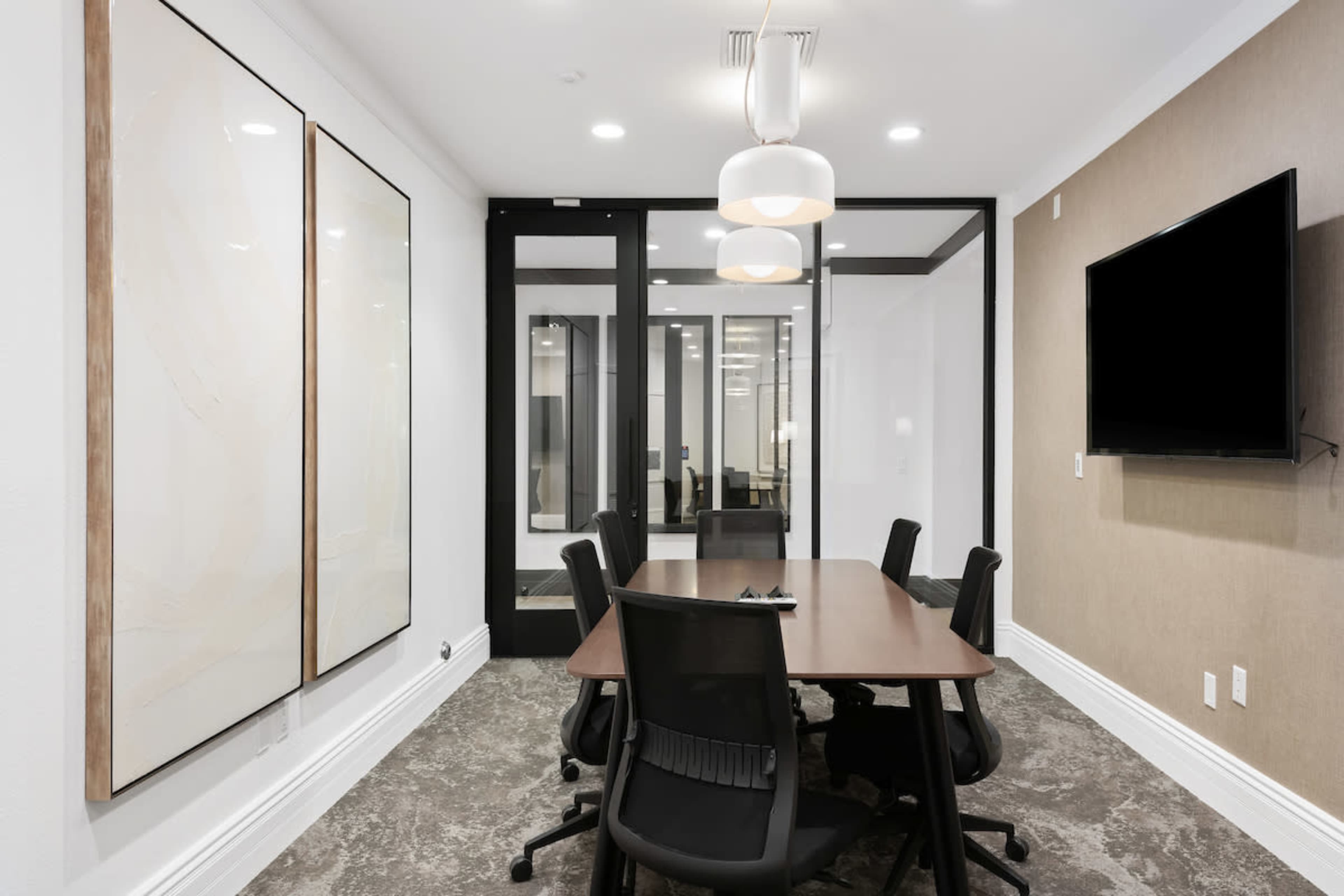 A modern conference room with a rectangular table, black chairs, and a large wall-mounted television.