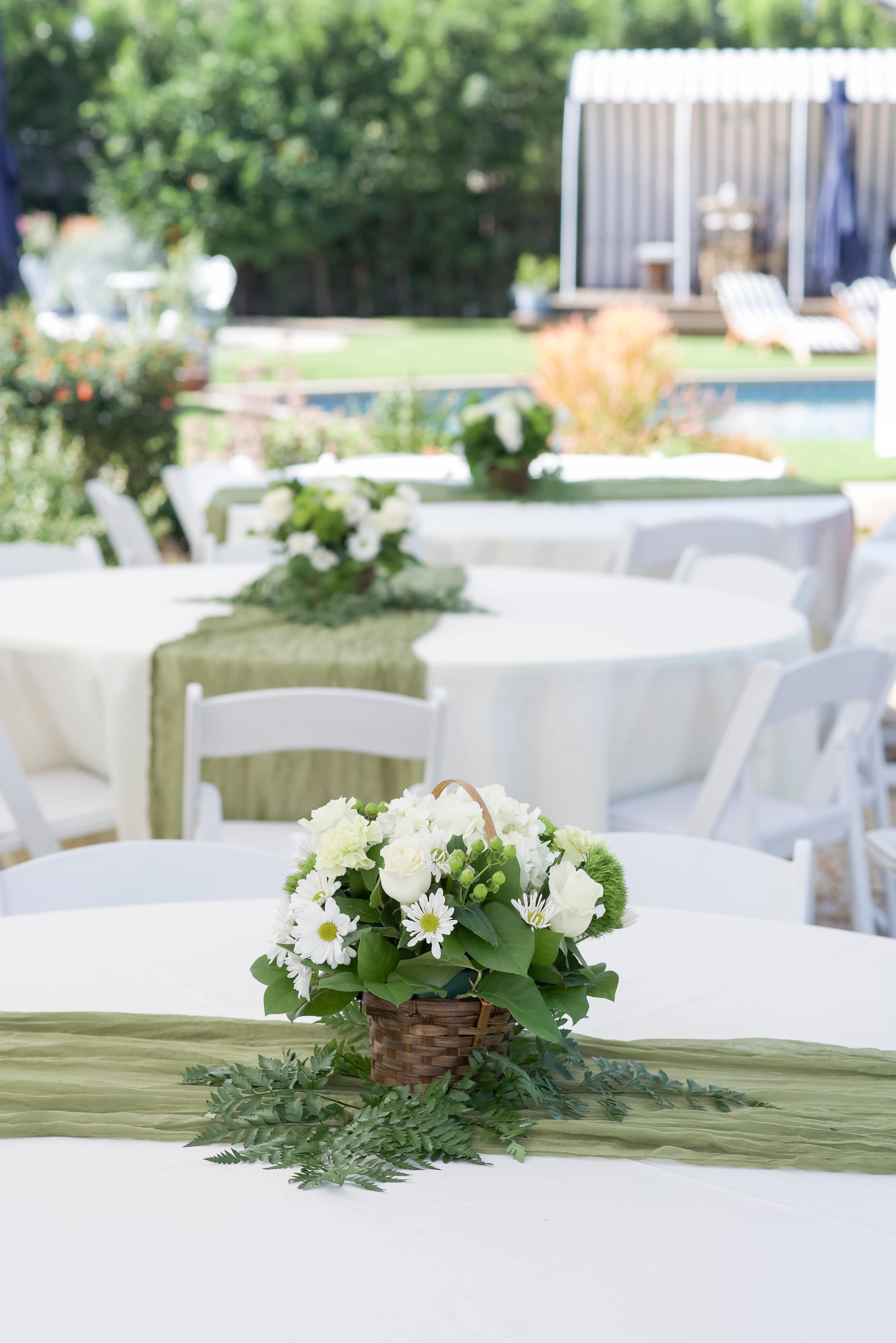 The image shows elegantly set tables with white tablecloths, each adorned with a basket of flowers at the center and a green table runner.