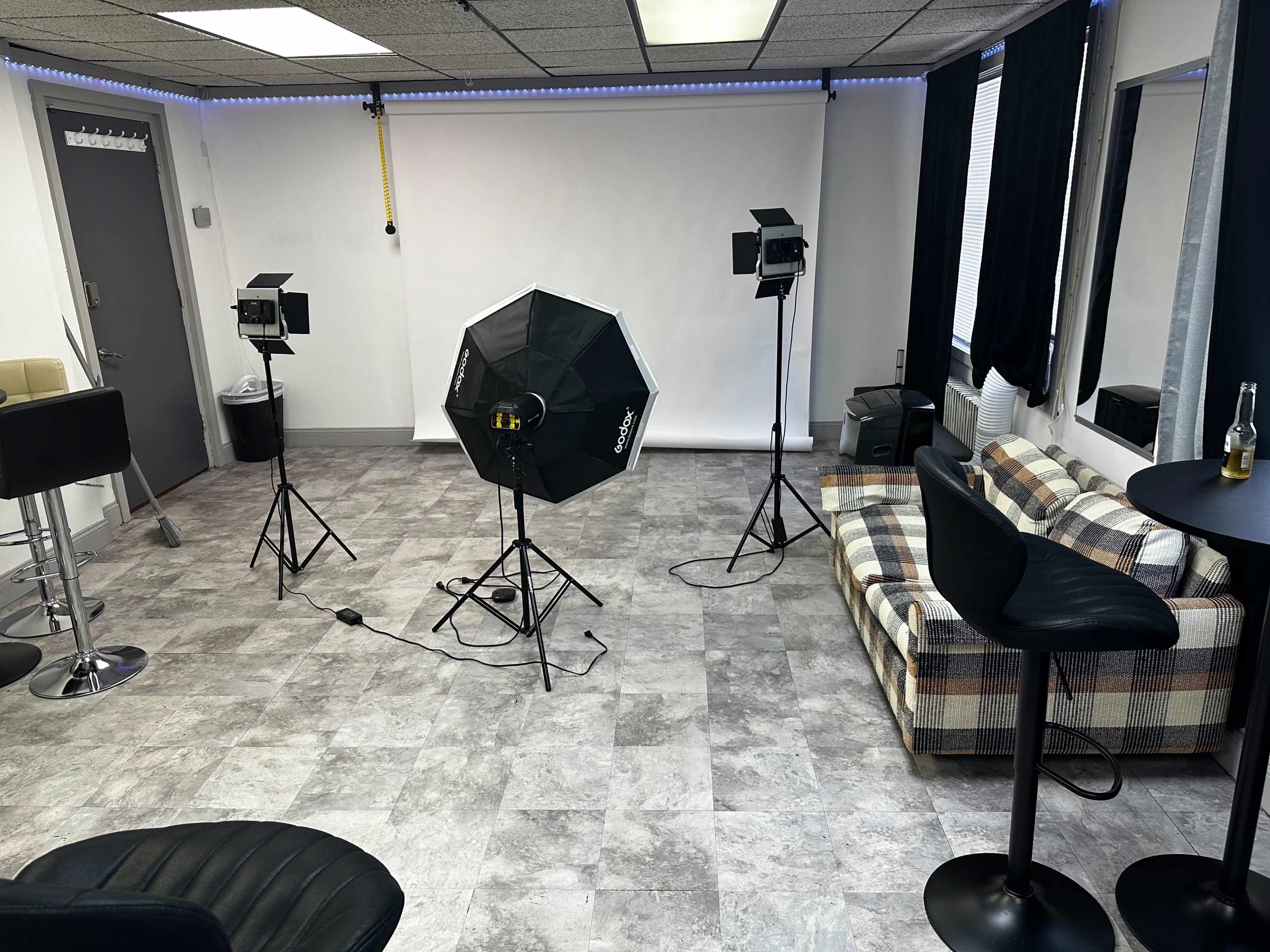 A photography studio setup with lighting equipment, a checkered sofa, and a small bar table.