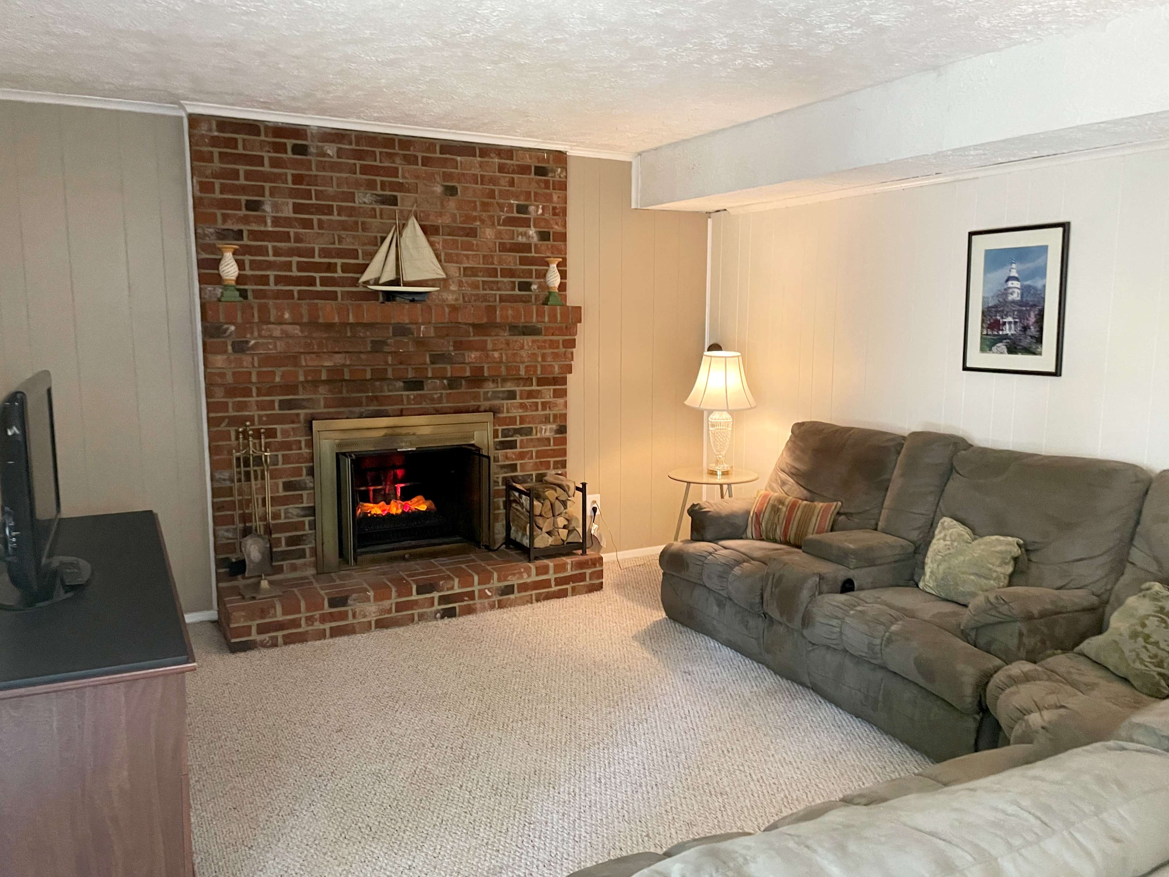 A living room with a brick fireplace, a television stand, a sectional couch, and a lamp beside the couch.