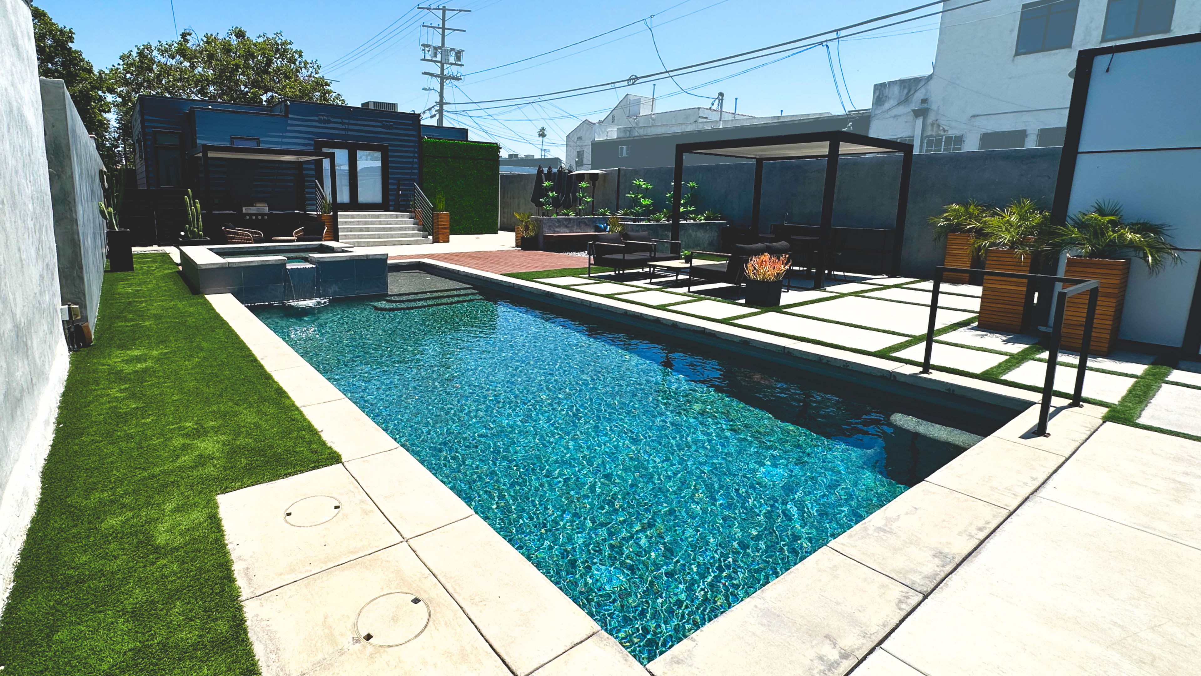 A modern backyard featuring a swimming pool, landscaped areas, patio seating, and a small outdoor structure.