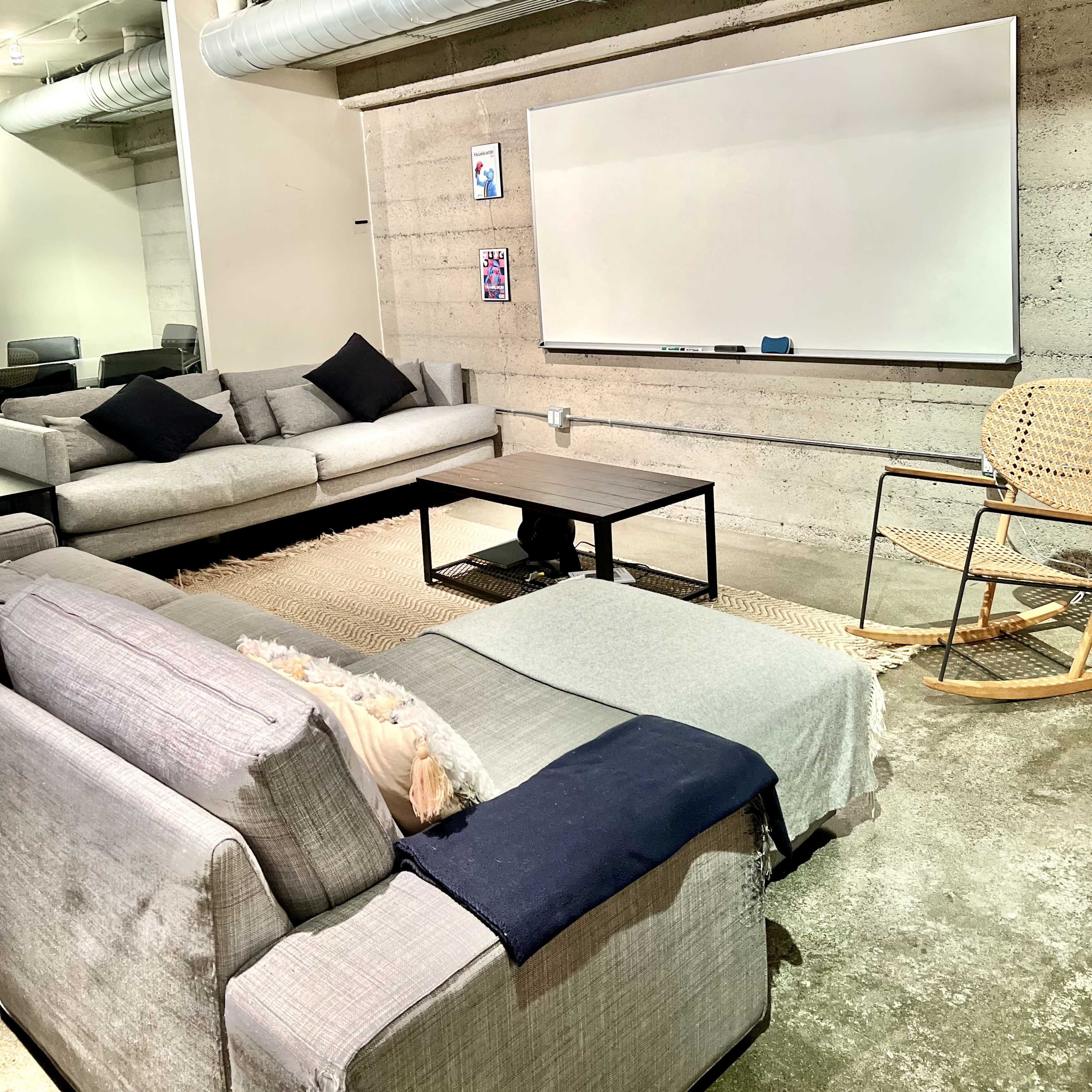 A modern, minimalistic lounge area featuring two sofas, a coffee table, a rocking chair, and a whiteboard on the wall.