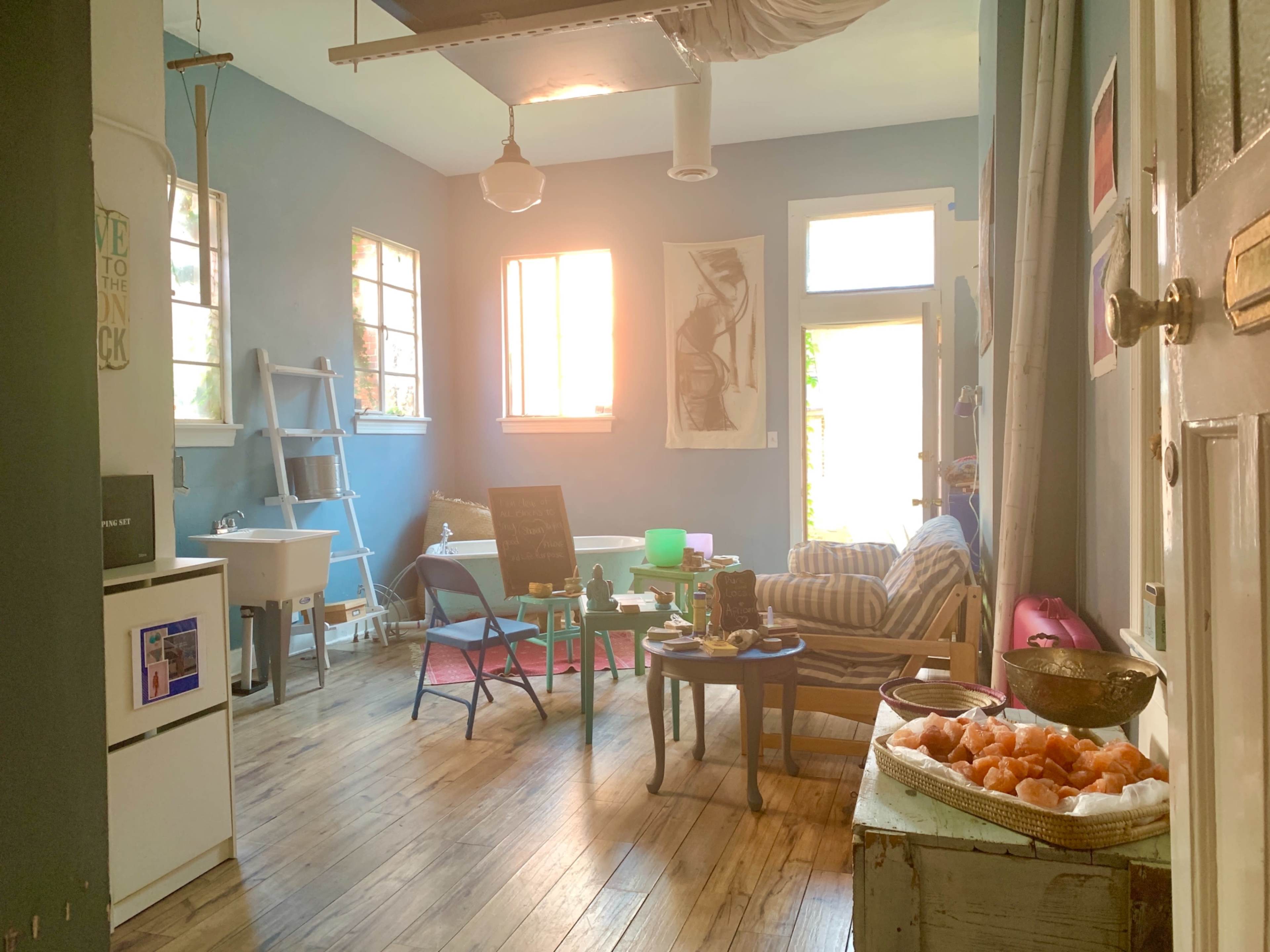 A brightly lit, cozy living space with a mix of furniture including a striped couch, a small table, and artwork on the walls.
