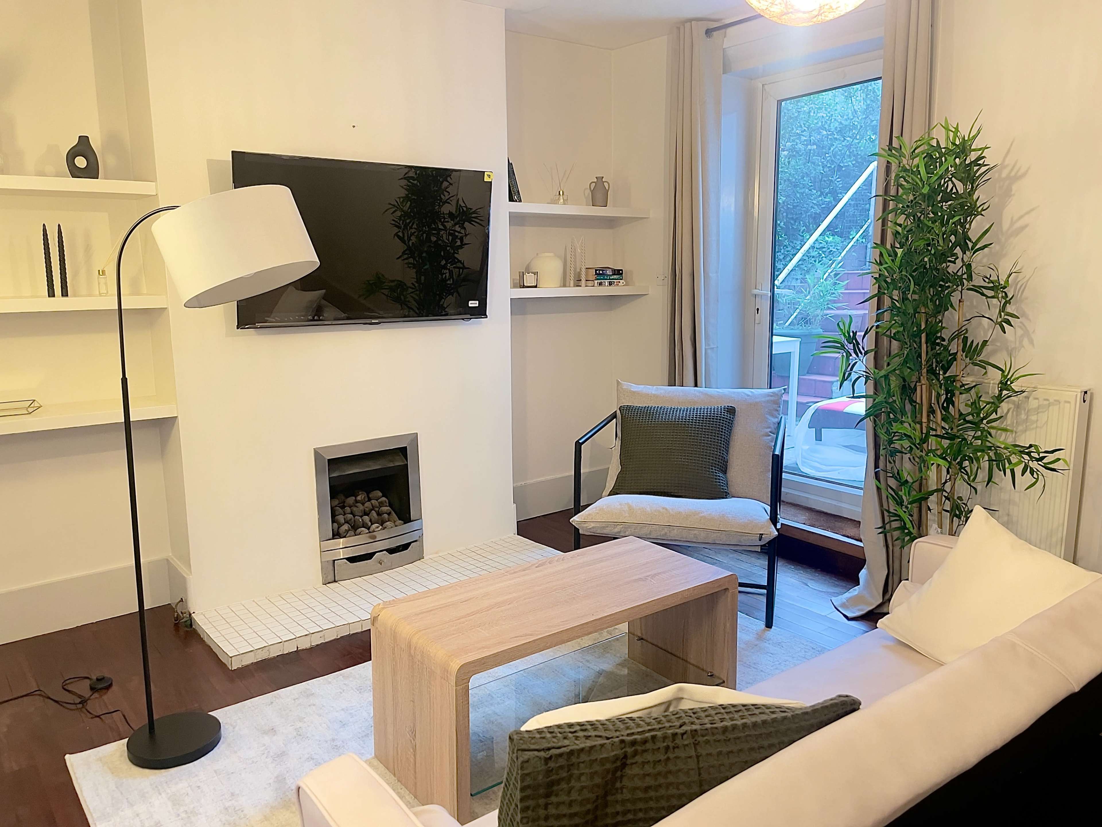 A modern living room features a television mounted on the wall, a floor lamp, a glass coffee table, and a sliding door that opens to a small balcony.