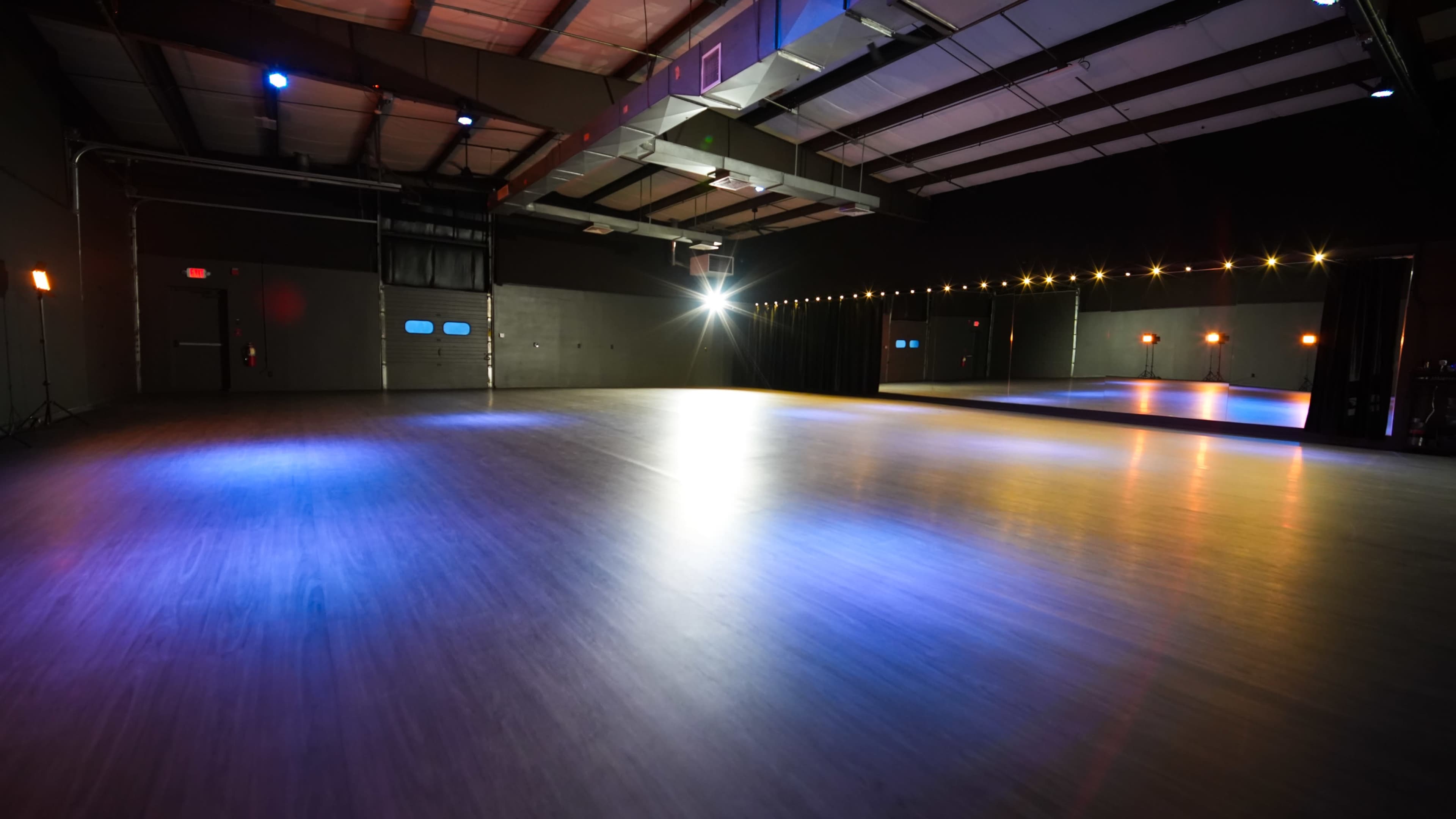 The image shows an empty dance studio with polished flooring, colored lights, and mirrors along one wall.