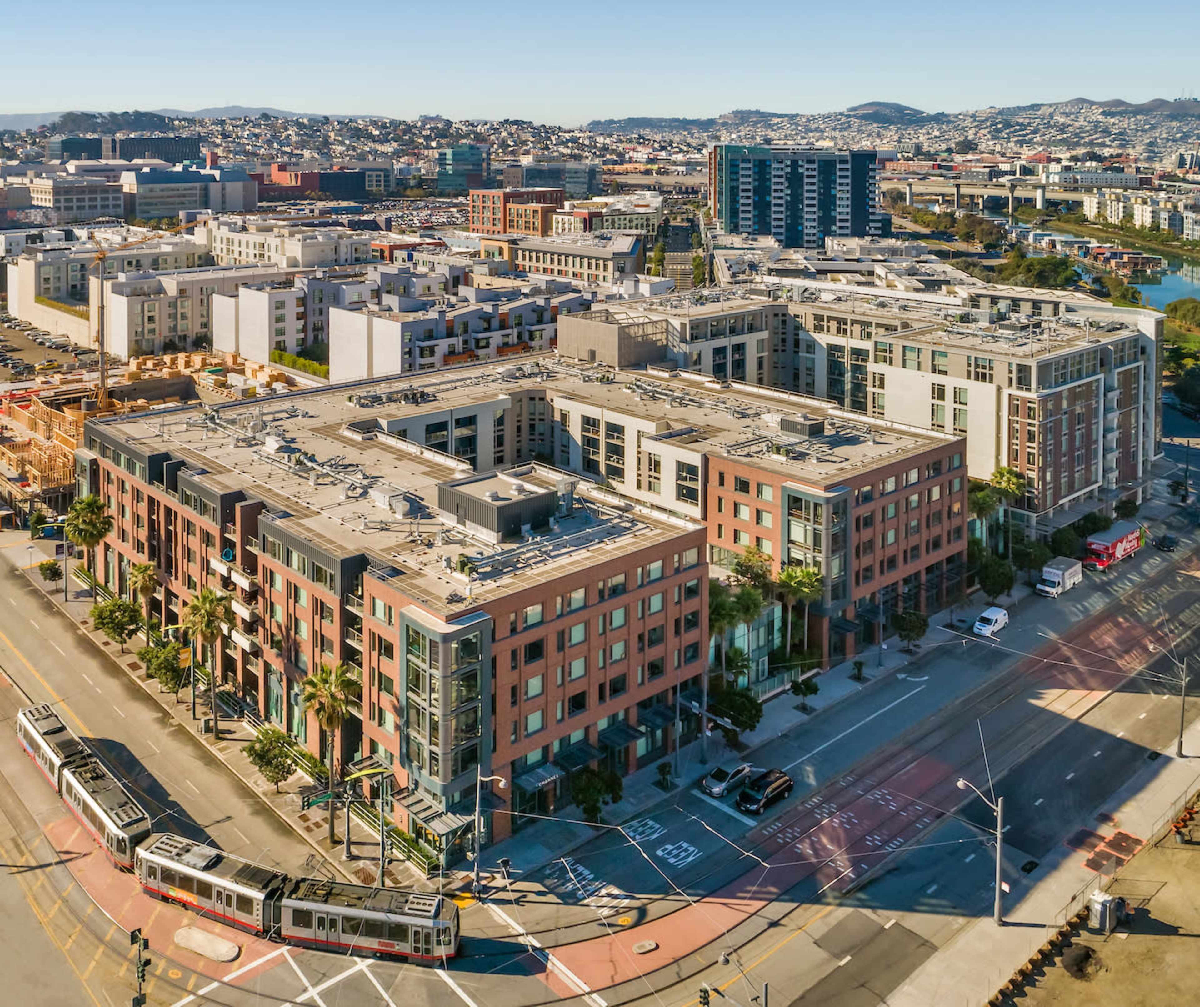 A sprawling urban area featuring several multi-story residential buildings, streets, and some construction sites, with distant hills in the background.