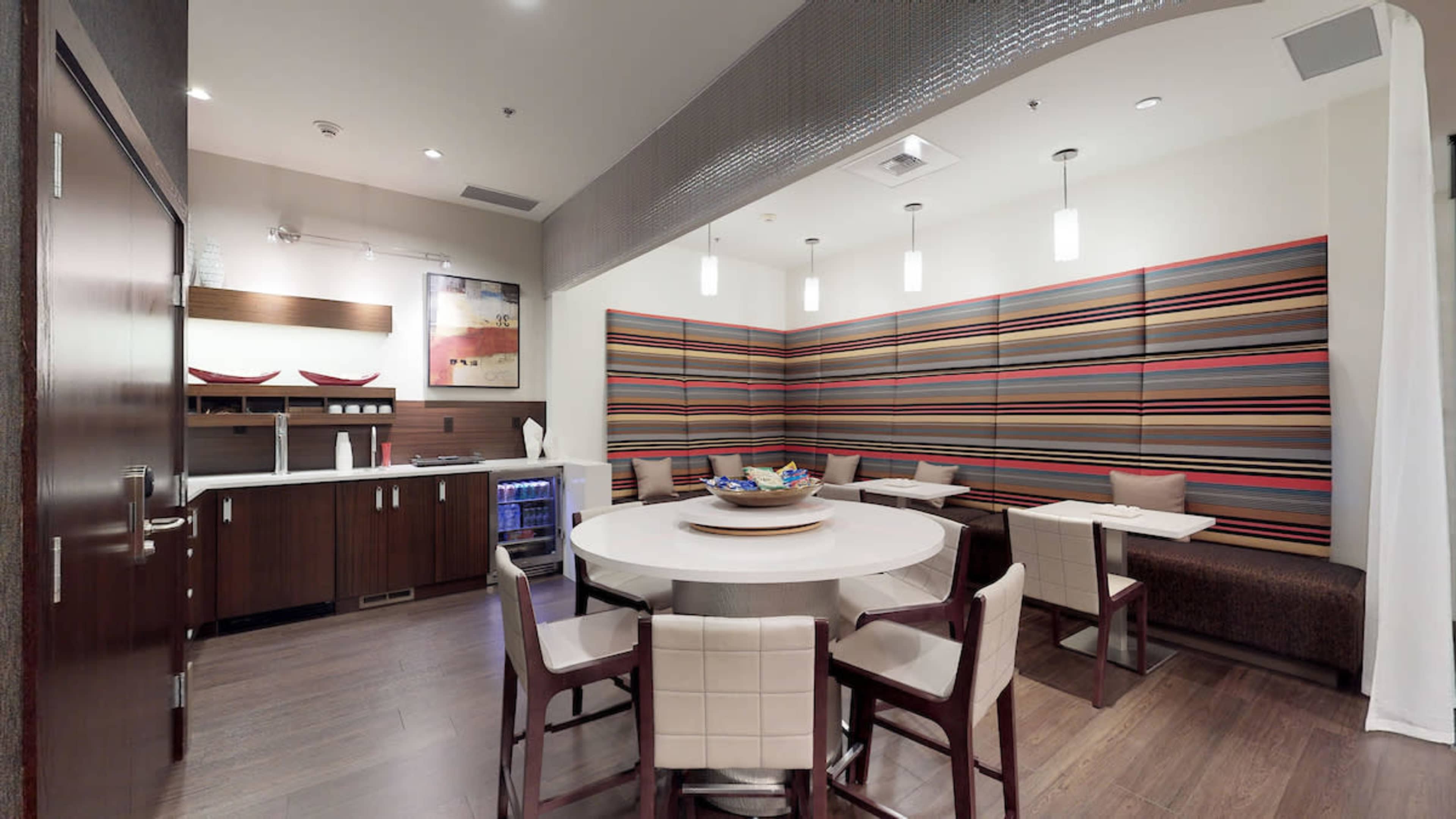 A modern dining area with a round table, light-colored chairs, and a patterned wall in a well-lit room.
