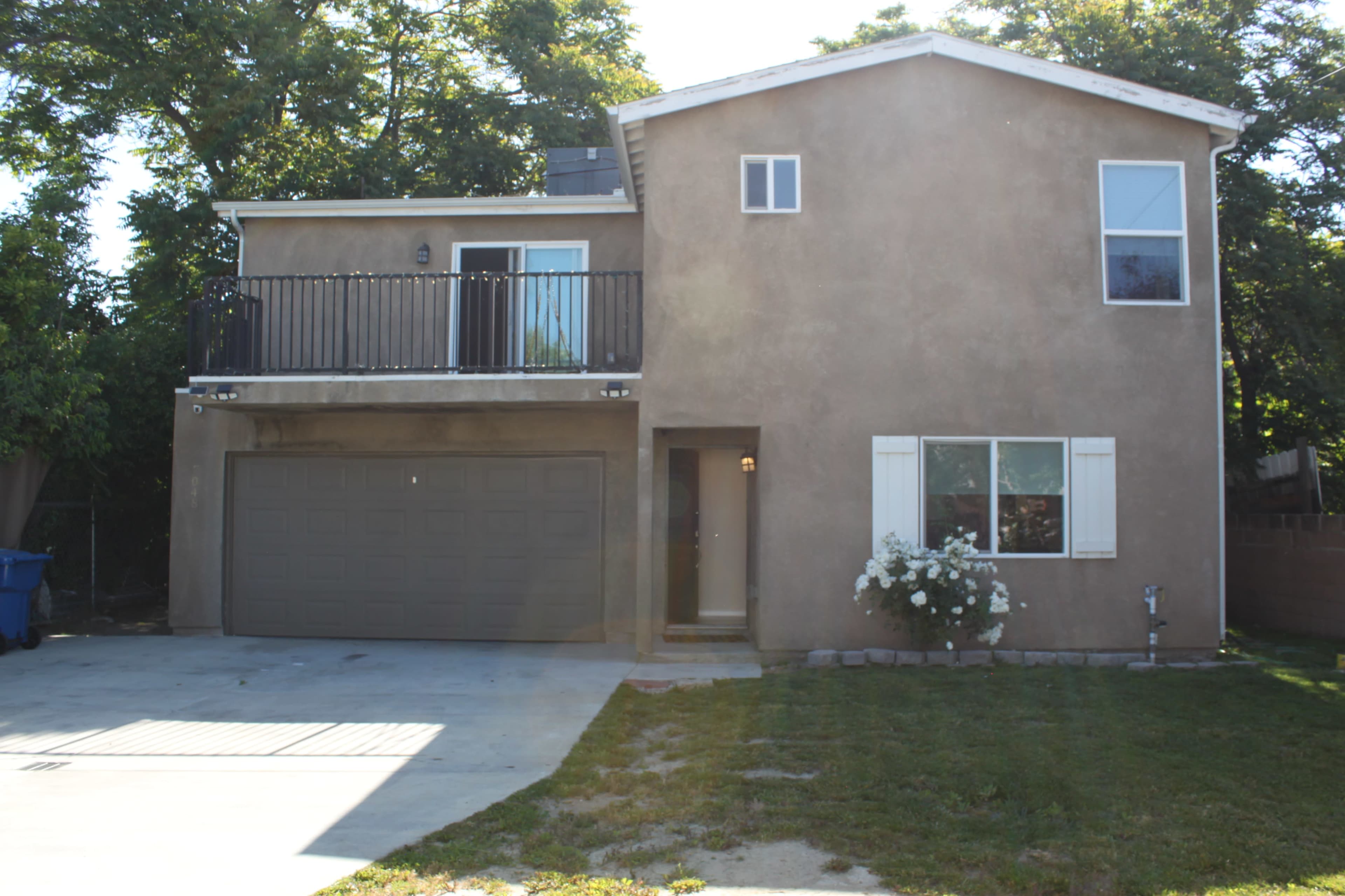 A two-story house features a balcony above a two-car garage, with a front yard and a paved driveway.
